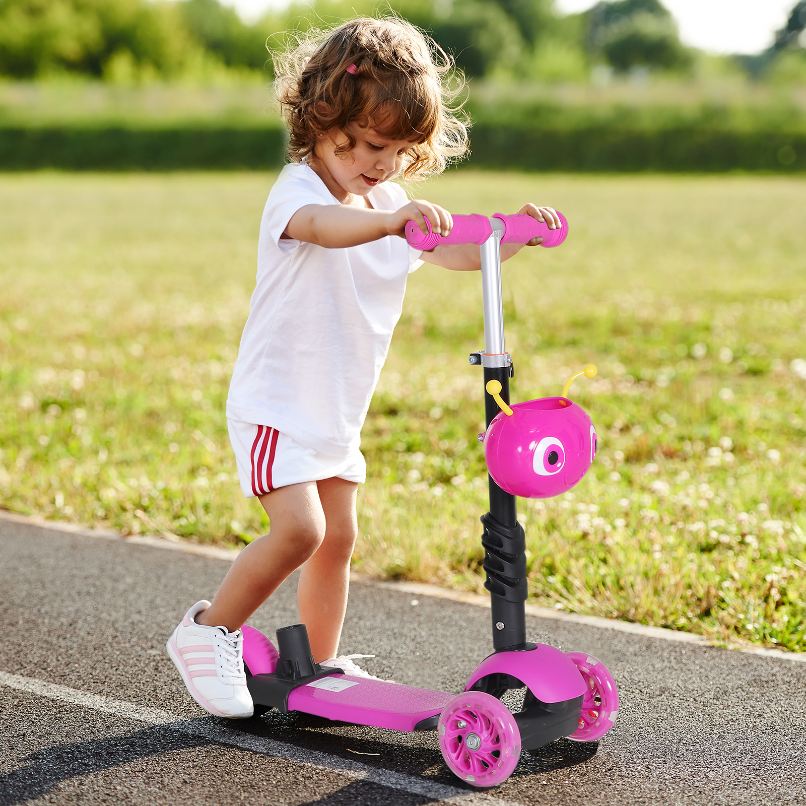 Bambina che guida un monopattino rosa a tre ruote su un sentiero asfaltato.