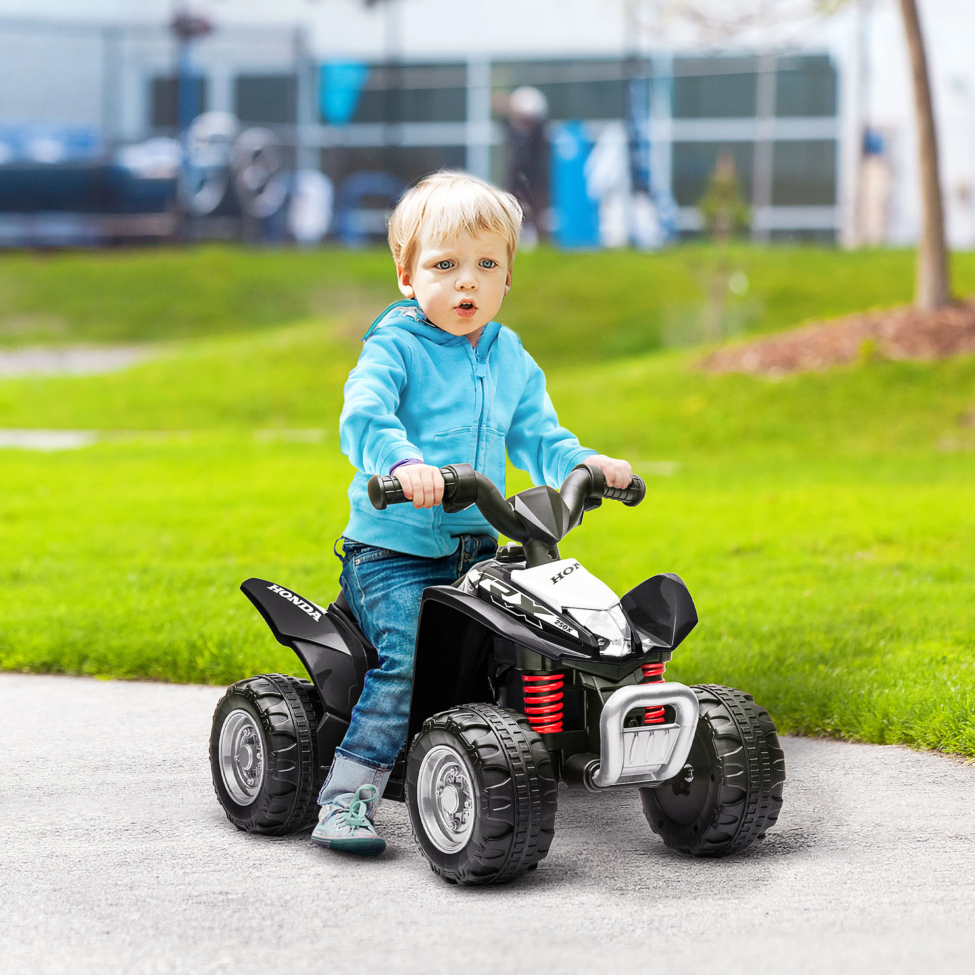Bambino con felpa blu guida un quad giocattolo nero su un sentiero asfaltato.