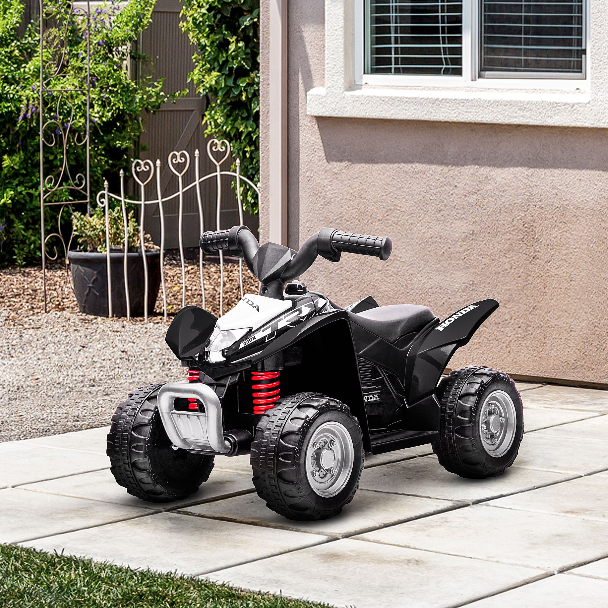 Un quad giocattolo nero Honda si trova su un patio pavimentato davanti a una casa con giardino.