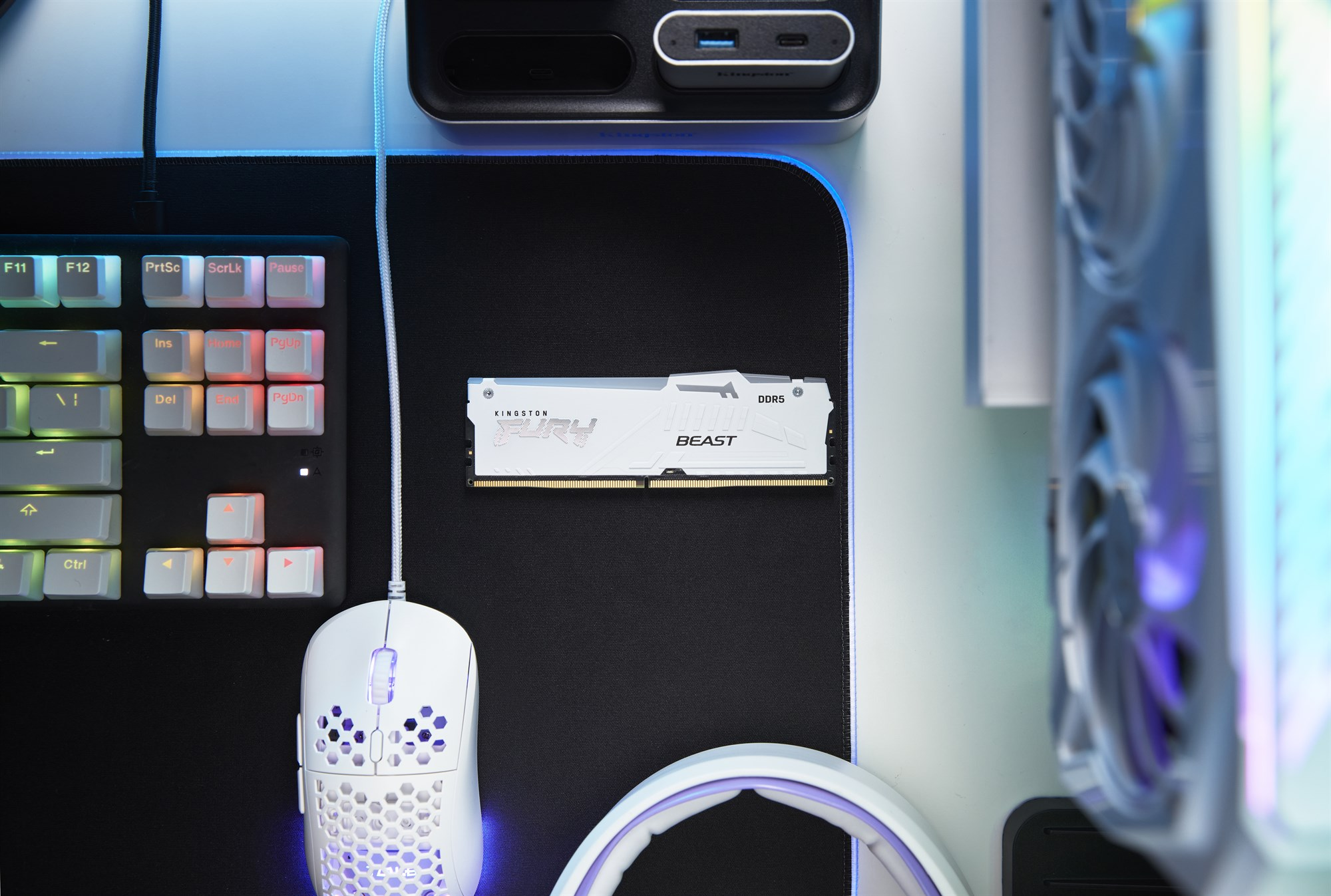 Biała kość pamięci RAM Kingston Fury DDR5 leży na czarnej podkładce obok klawiatury, myszy i komputera.