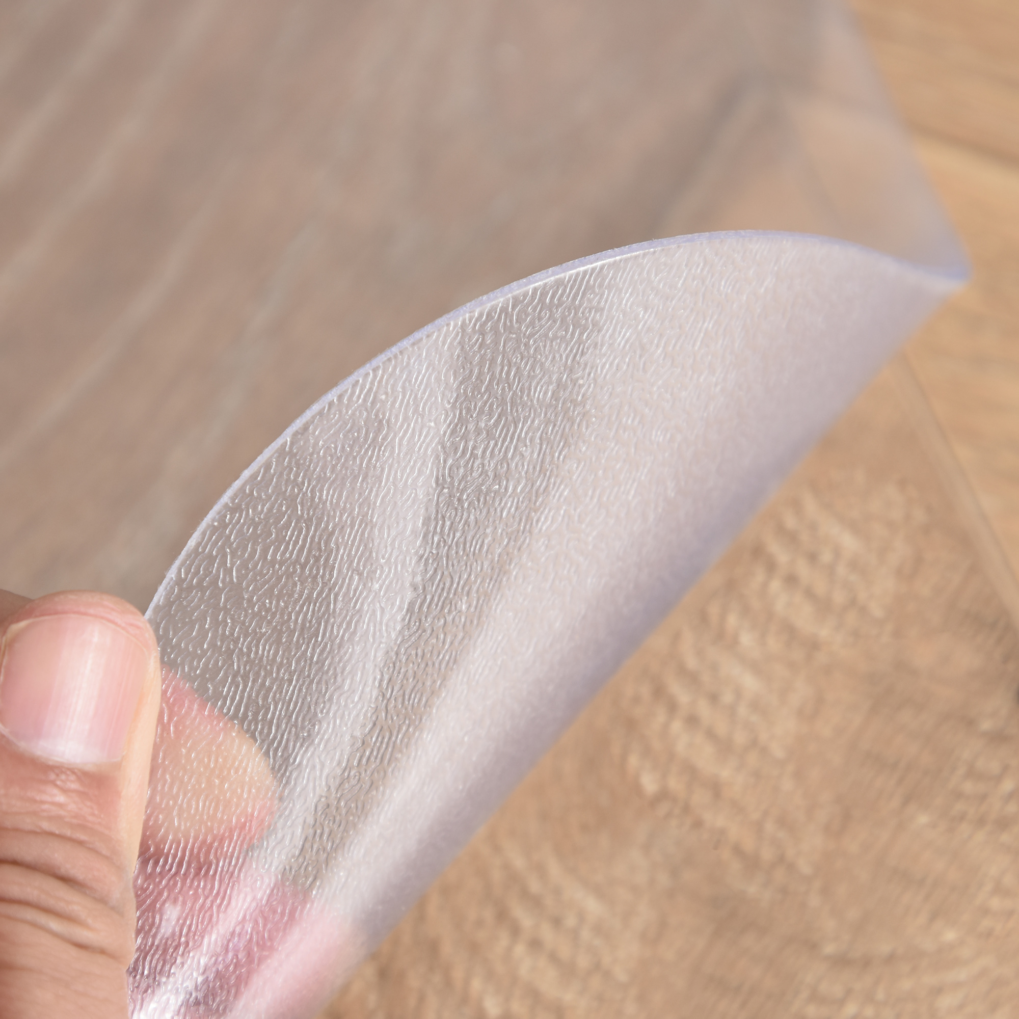 Una mano dobla una estera de plástico transparente y texturizada sobre un suelo de madera.