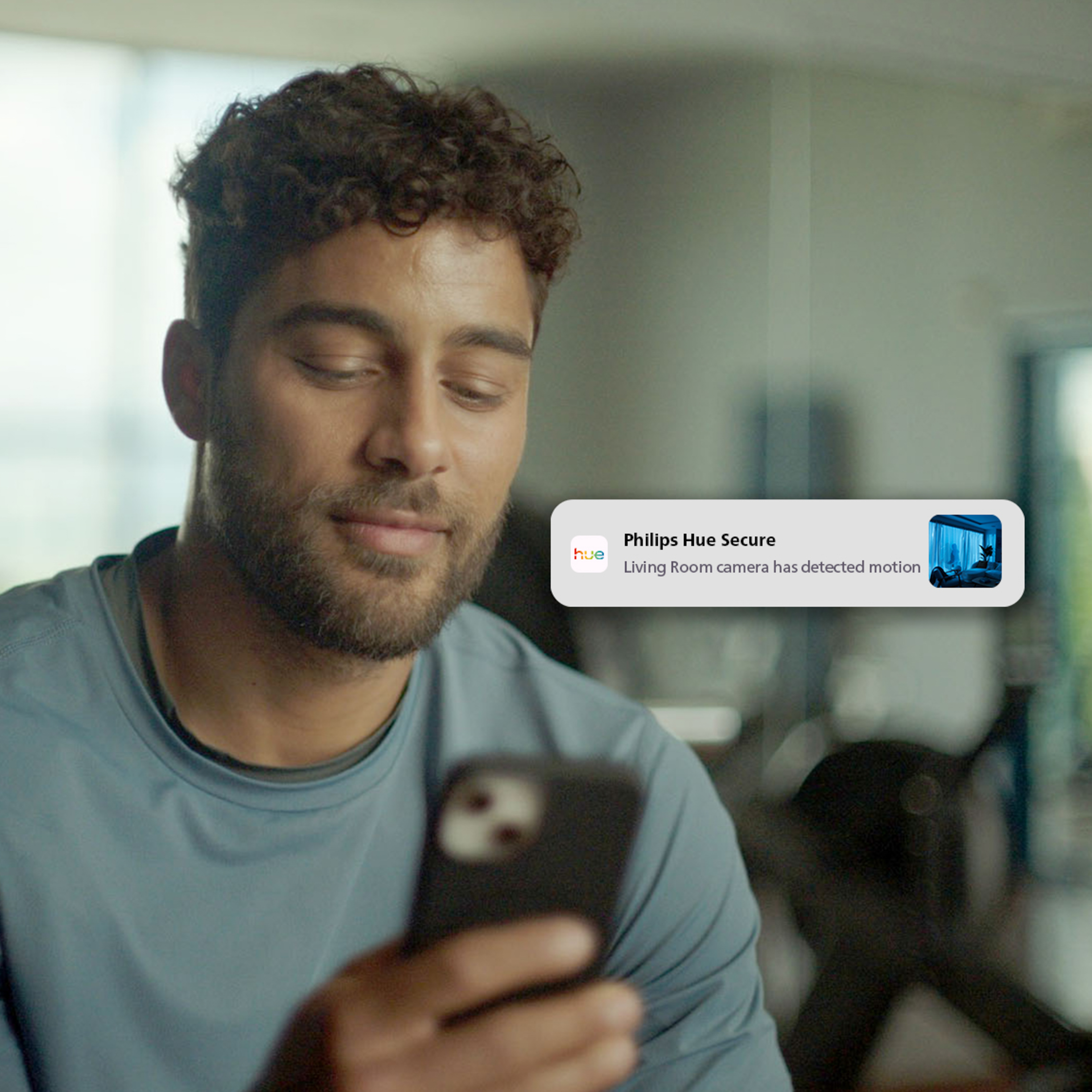 Ein Mann mit dunkelgelocktem Haar schaut auf sein Smartphone mit einer Philips Hue Secure Bewegungsmeldung.