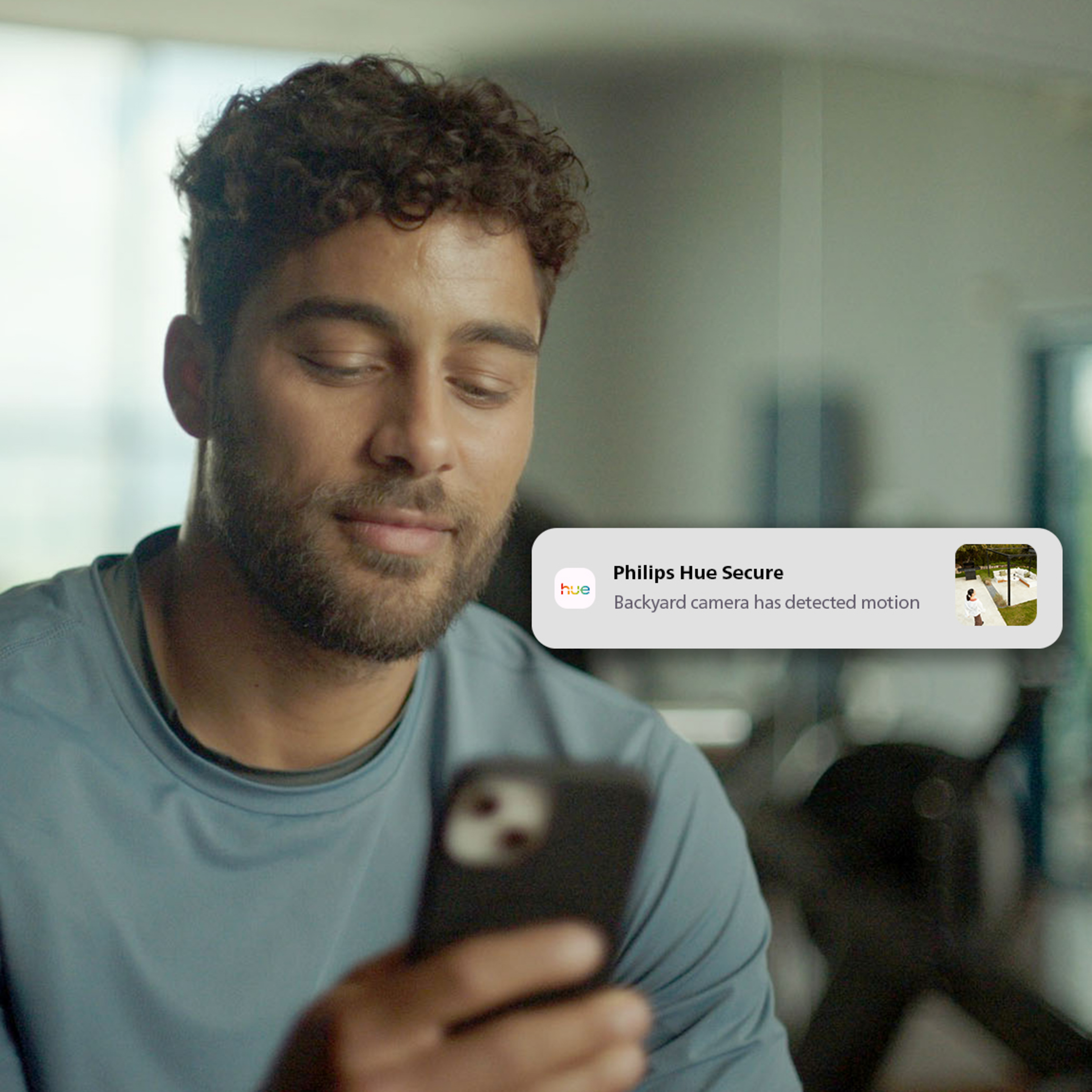 Un hombre con pelo rizado mira su smartphone mostrando una notificación de movimiento de Philips Hue Secure.
