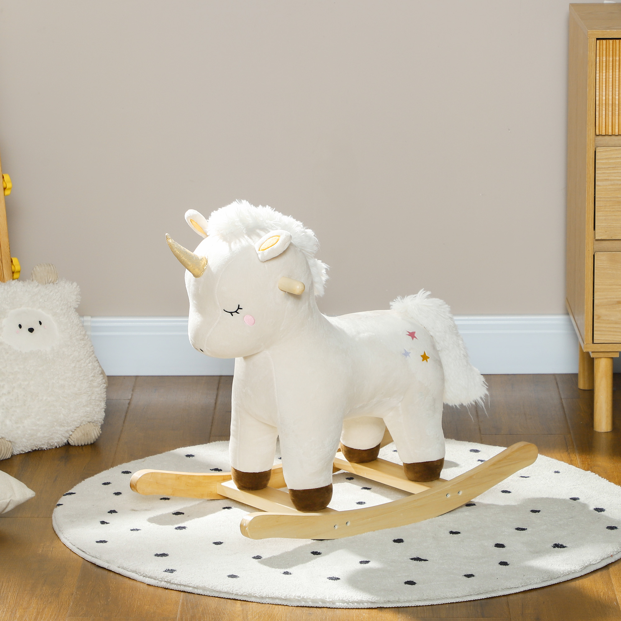 Un cavallo a dondolo unicorno bianco di peluche con dondoli di legno su un tappeto rotondo a pois.