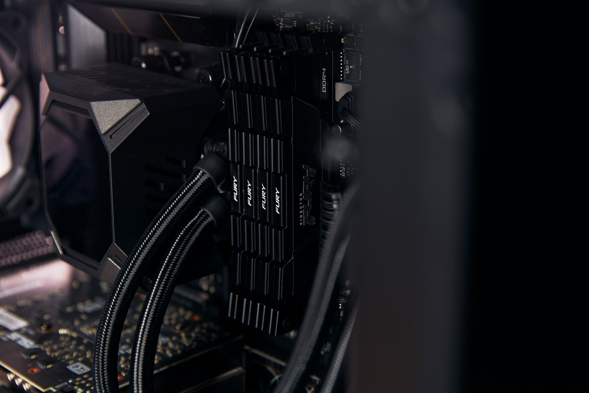 Zbliżenie czterech czarnych modułów RAM Kingston Fury w komputerze, obok chłodzenia z rurkami.