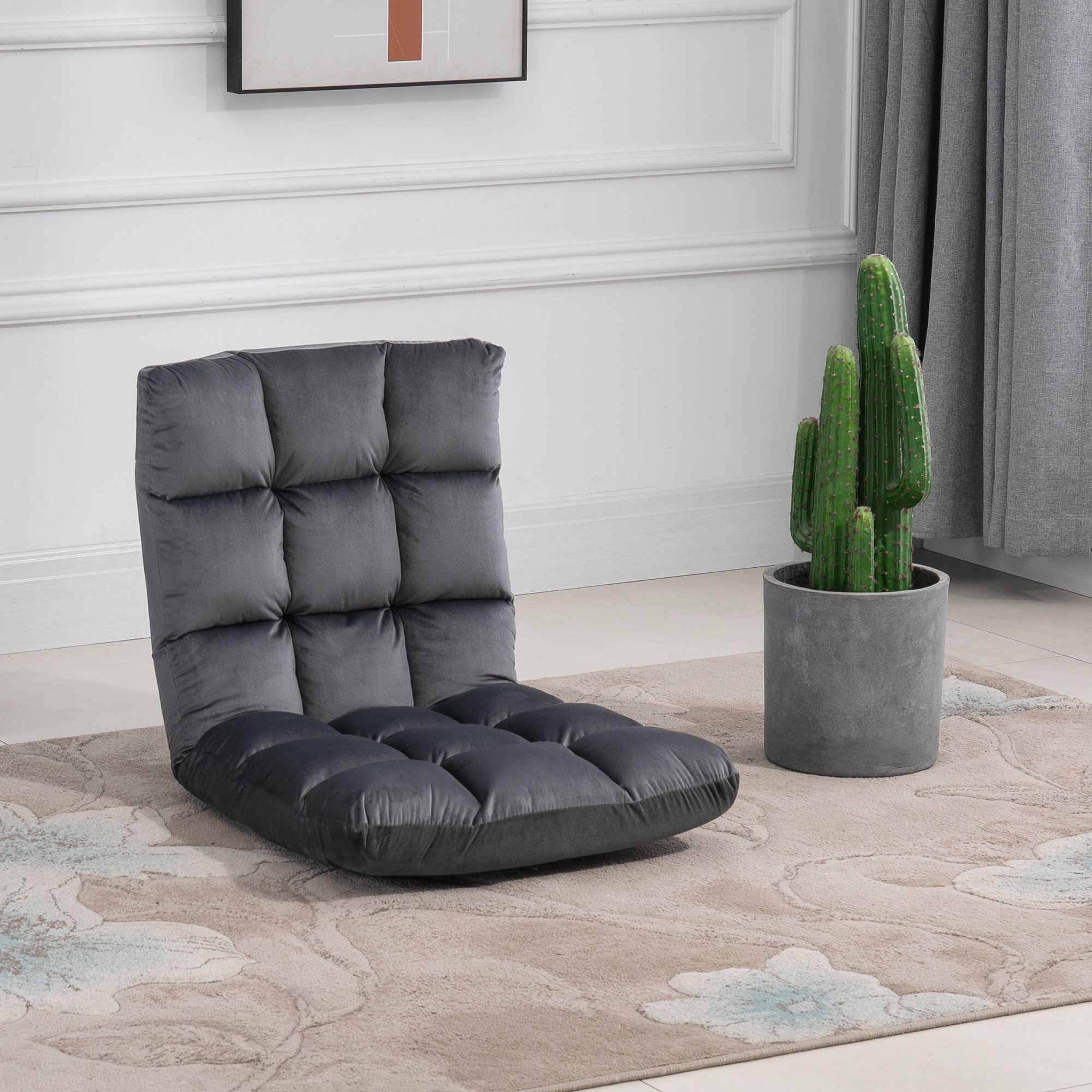 Una poltrona da pavimento grigia trapuntata si trova su un tappeto fantasia accanto a un cactus in vaso.