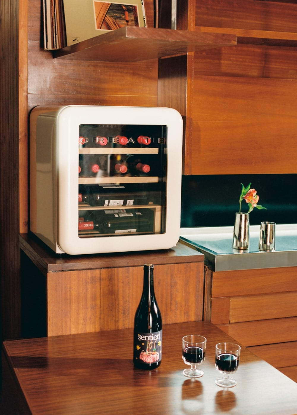 Una vinoteca blanca sobre muebles de madera junto a dos copas de vino y una botella.