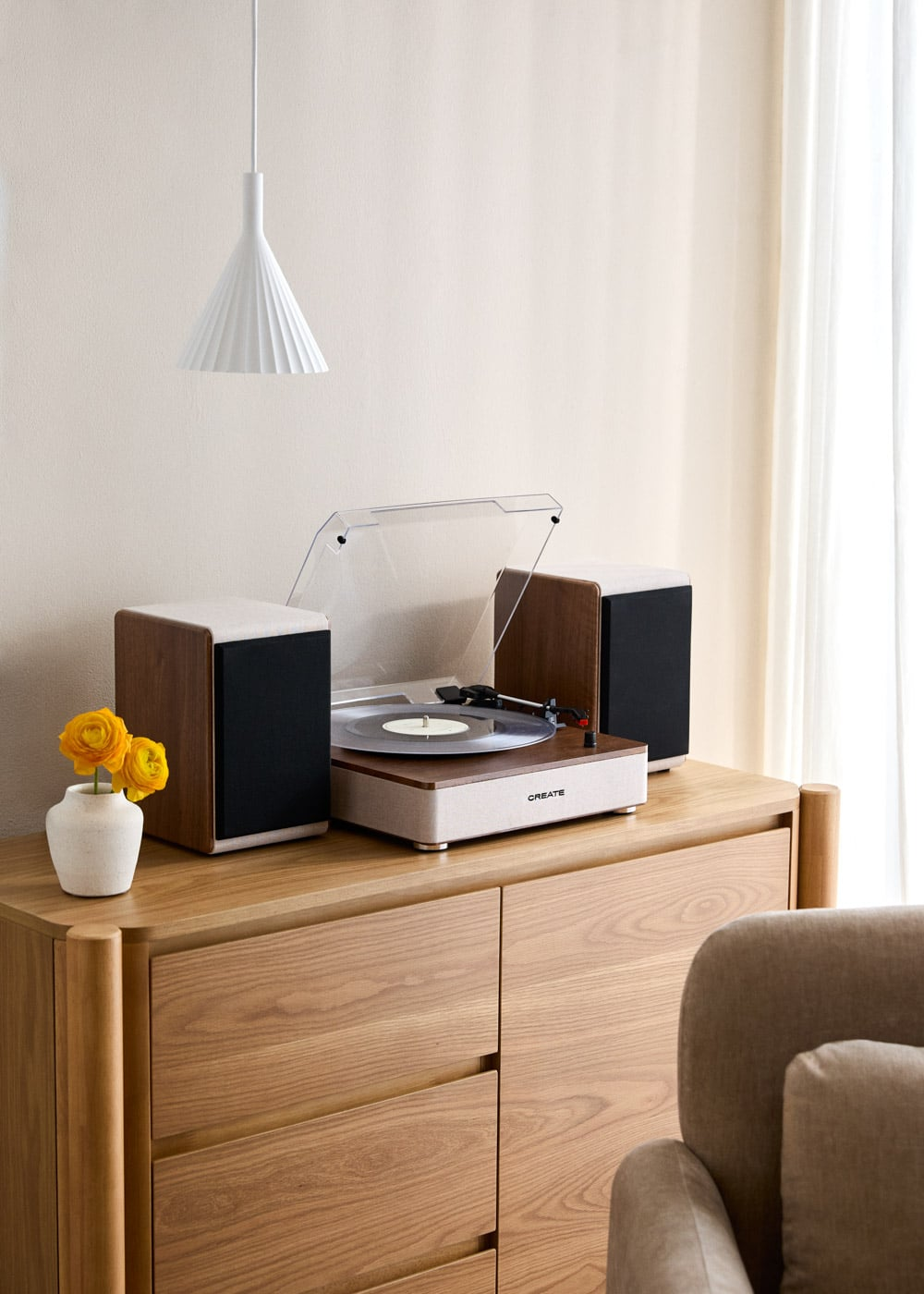 Un tocadiscos con dos altavoces en un armario de madera, al lado de un florero blanco con flores amarillas.