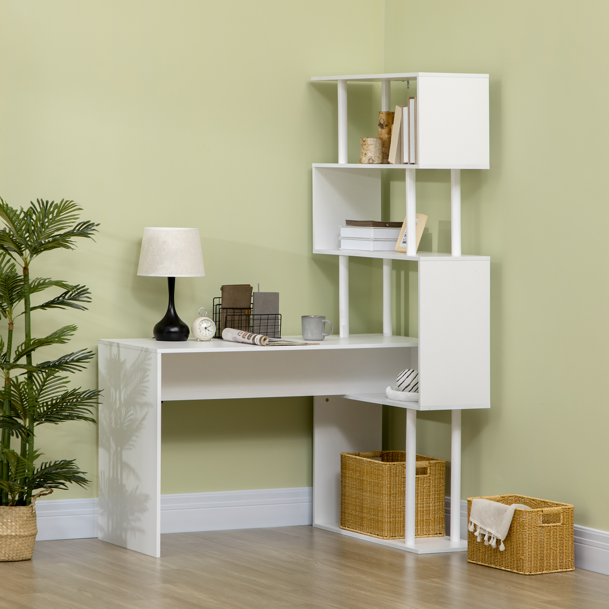Una scrivania bianca a L con libreria su una parete verde, con lampada, libri e cestini.