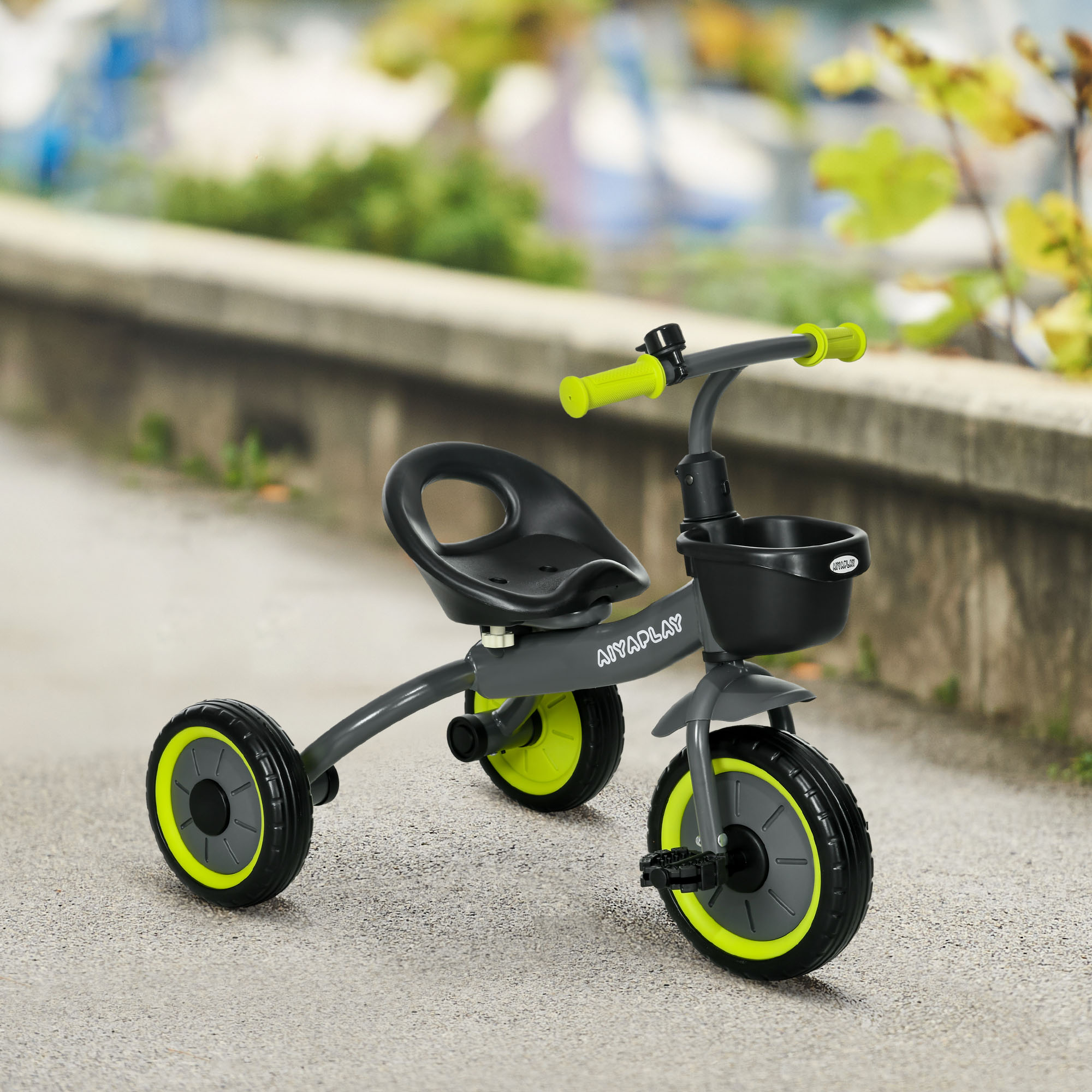 Un triciclo per bambini grigio con accenti verdi si trova su un marciapiede.
