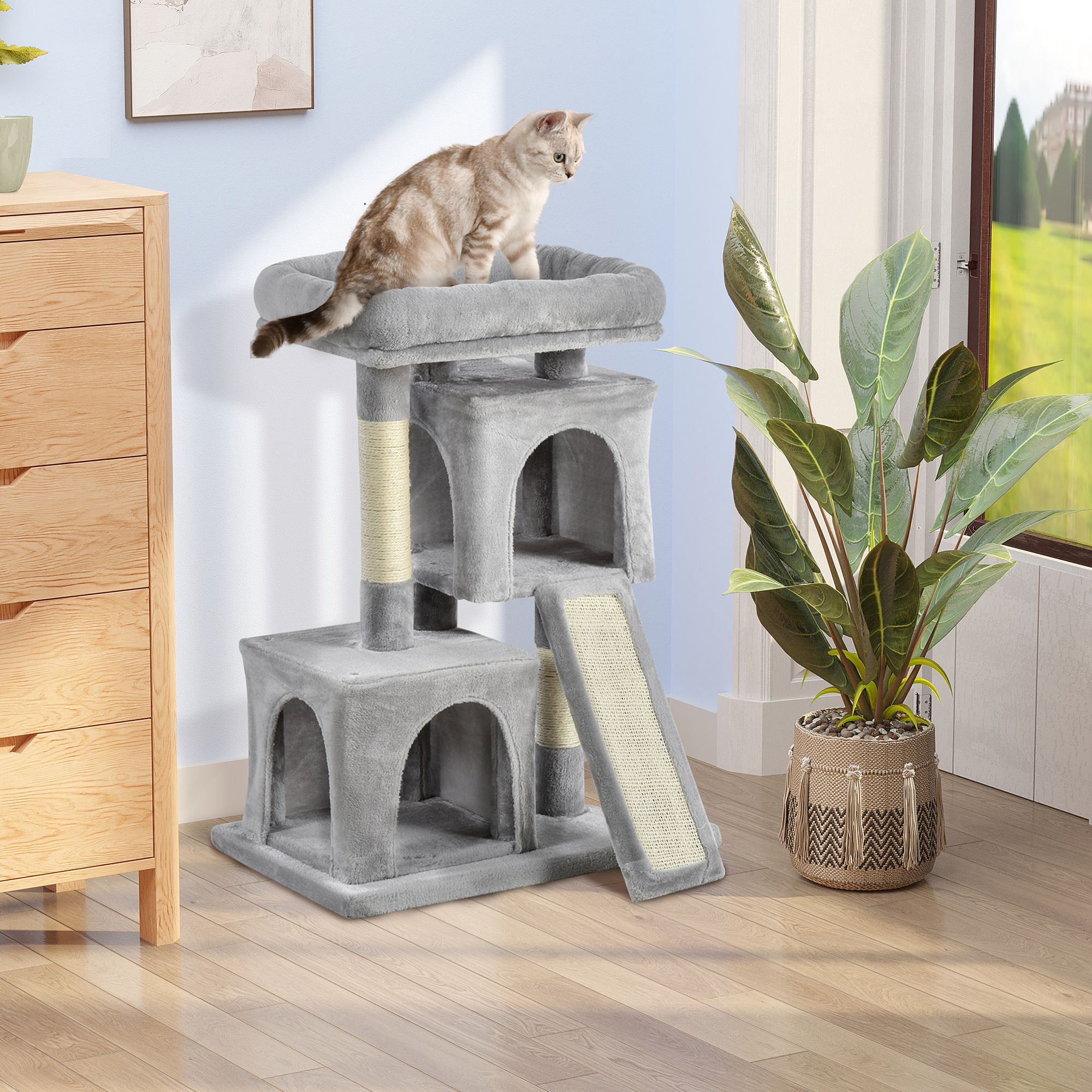 Un tiragraffi grigio con un gatto sopra, accanto a un comò in legno e a una grande pianta in vaso.