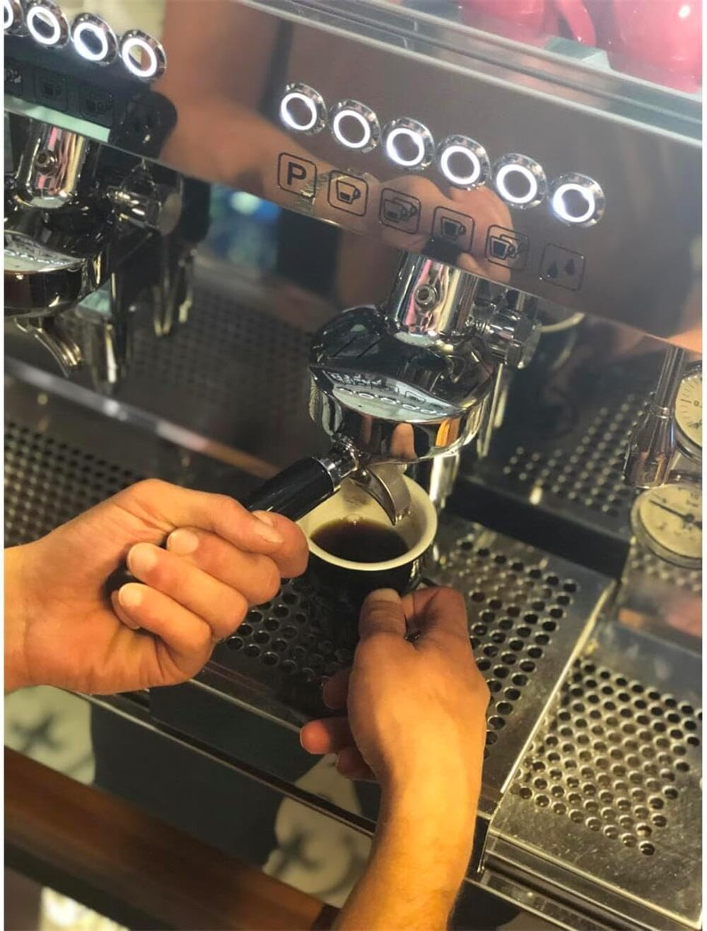 Un barista opera una máquina de espresso de cromo, preparando café en una taza pequeña.