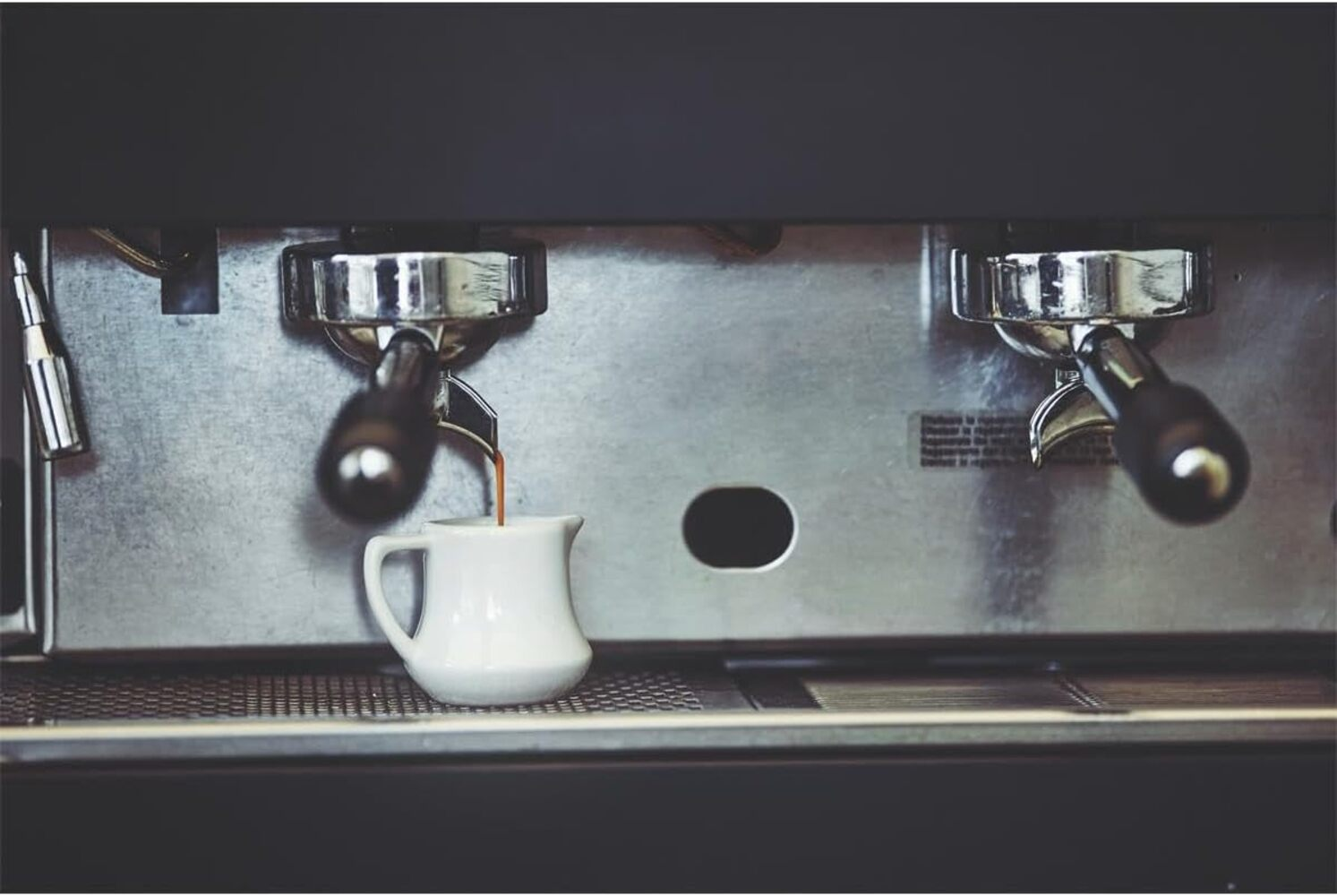 Una máquina de espresso vierte café en una pequeña jarra blanca sobre la bandeja.