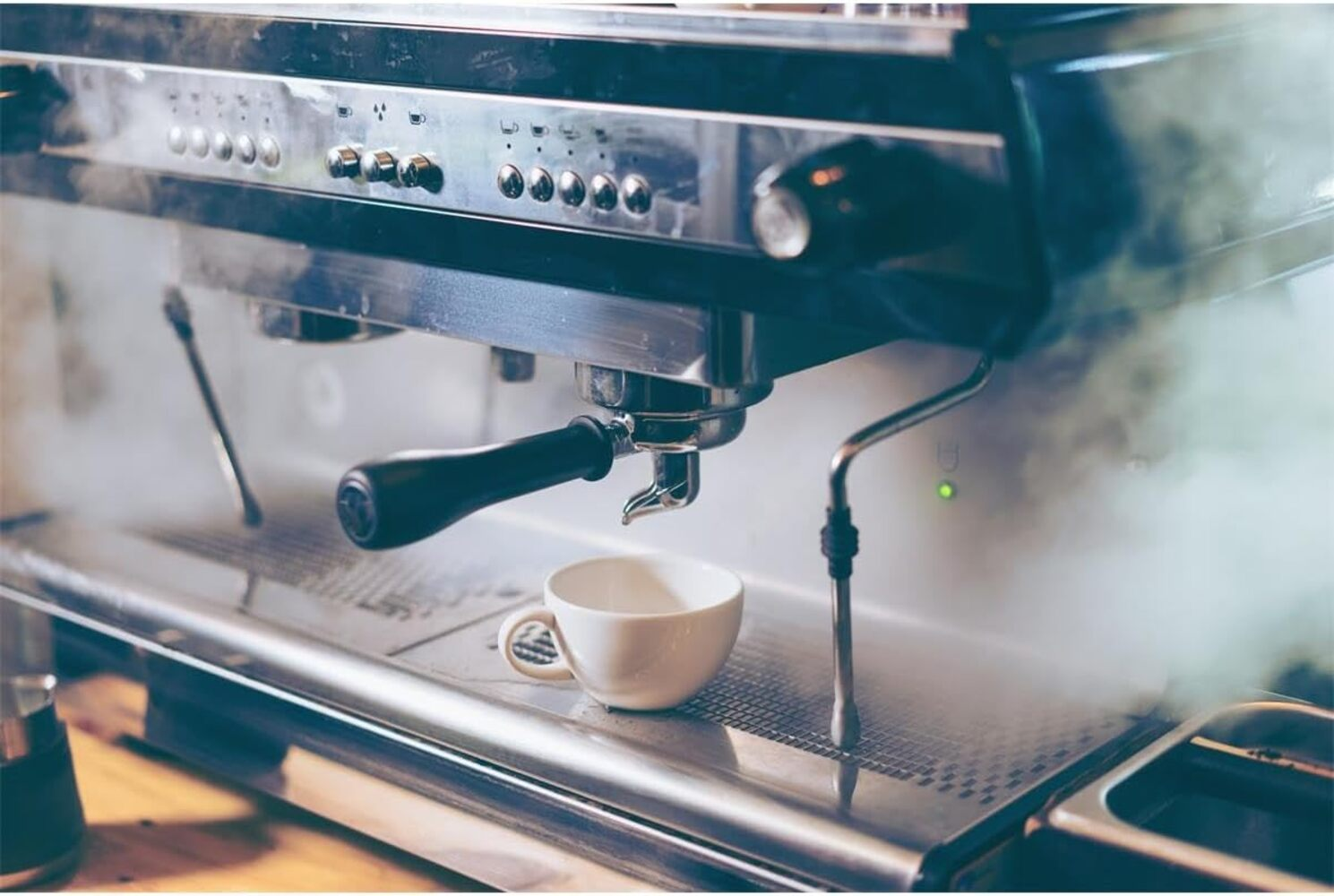 Una cafetera exprés profesional de acero inoxidable emite vapor mientras una taza blanca reposa en la bandeja.
