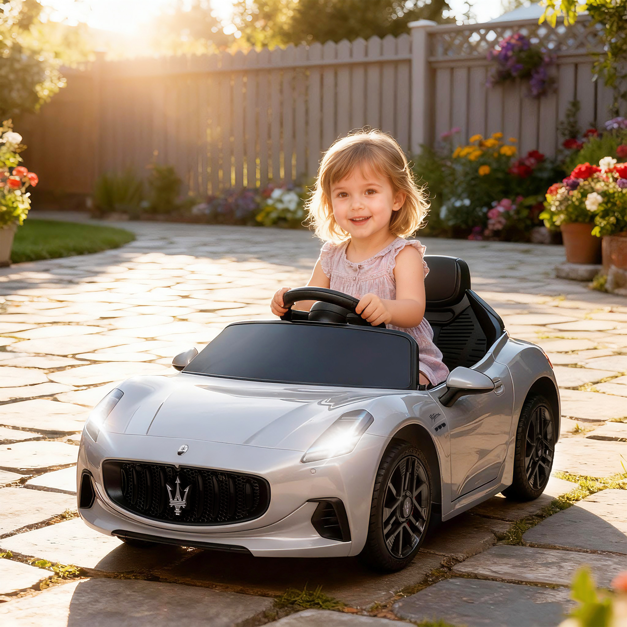 Bambina sorridente seduta su un'auto giocattolo argentata in un patio soleggiato.