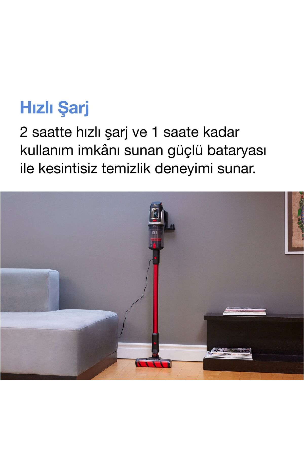 Gri duvar önünde kanepe yanında duran kırmızı şarjlı dikey süpürge.