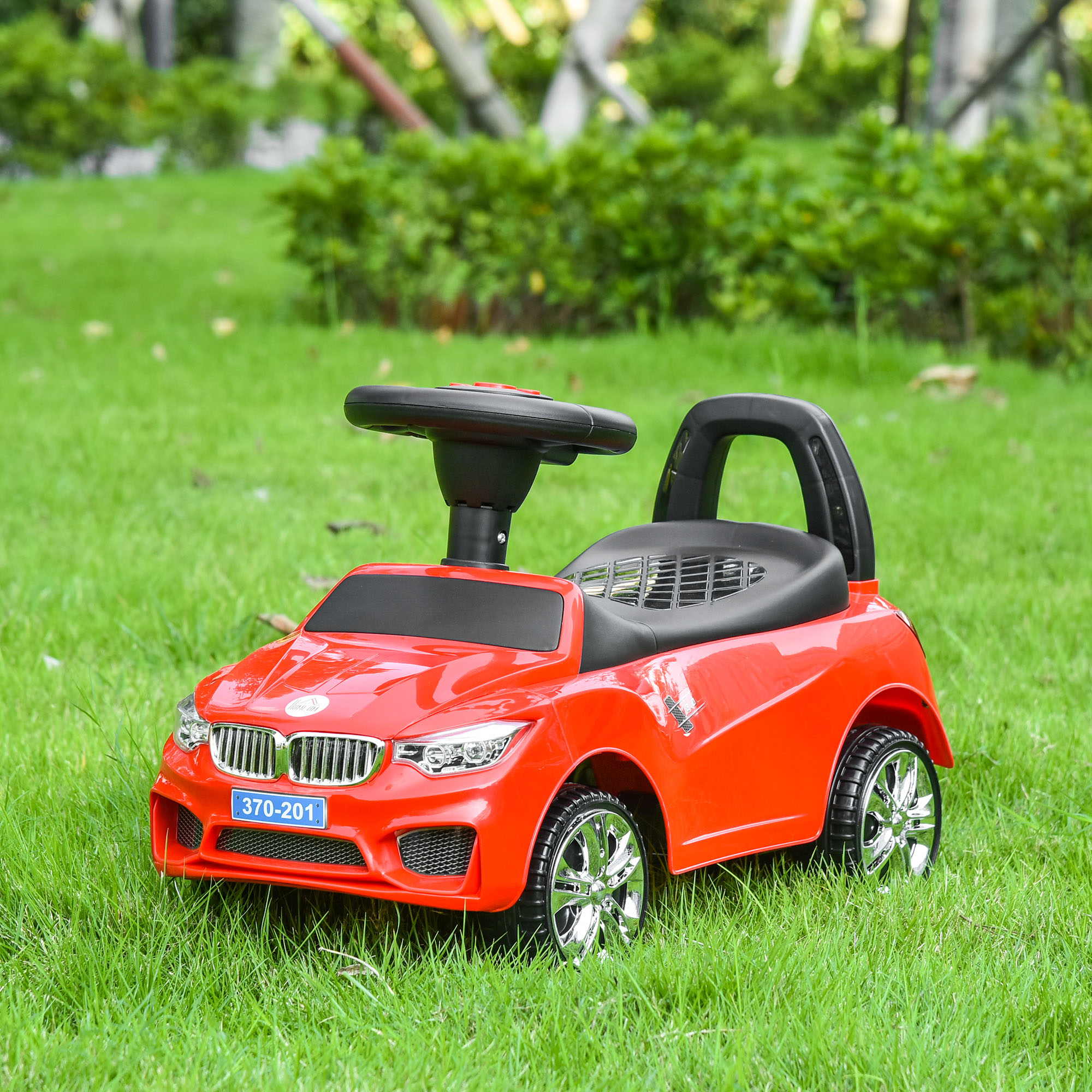 Un'auto giocattolo rosso vivo è parcheggiata su un prato verde con sfondo sfocato.