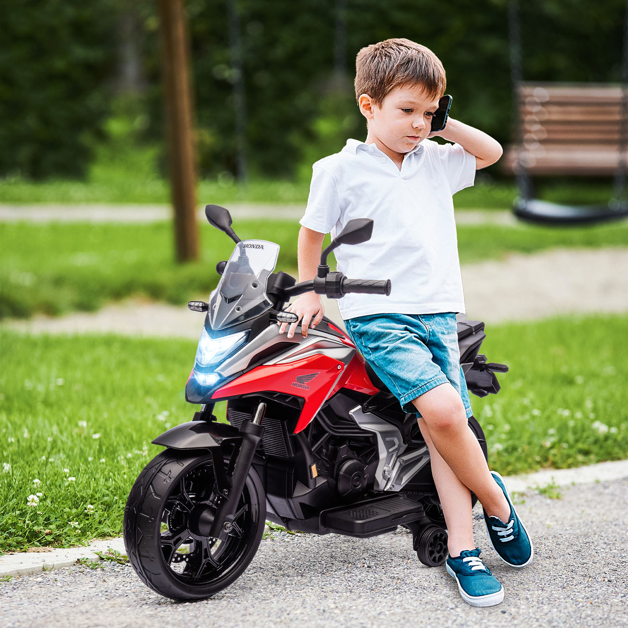 Un bambino con una camicia bianca parla al telefono seduto su una moto giocattolo rossa e nera.