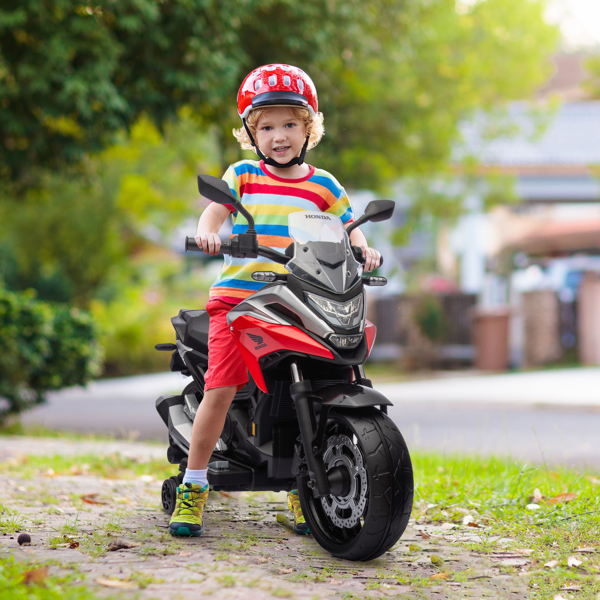 Un bambino con casco rosso guida una moto giocattolo rossa e nera all'aperto.