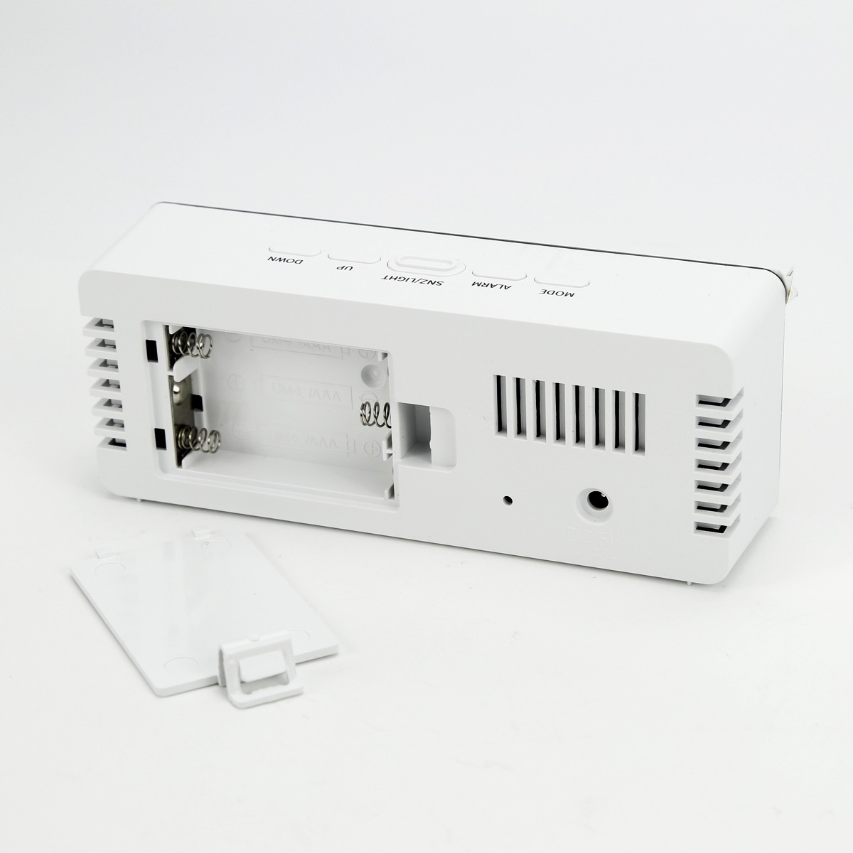 Rückseite einer weißen Digitaluhr mit geöffnetem Batteriefach und abgenommener Abdeckung.
