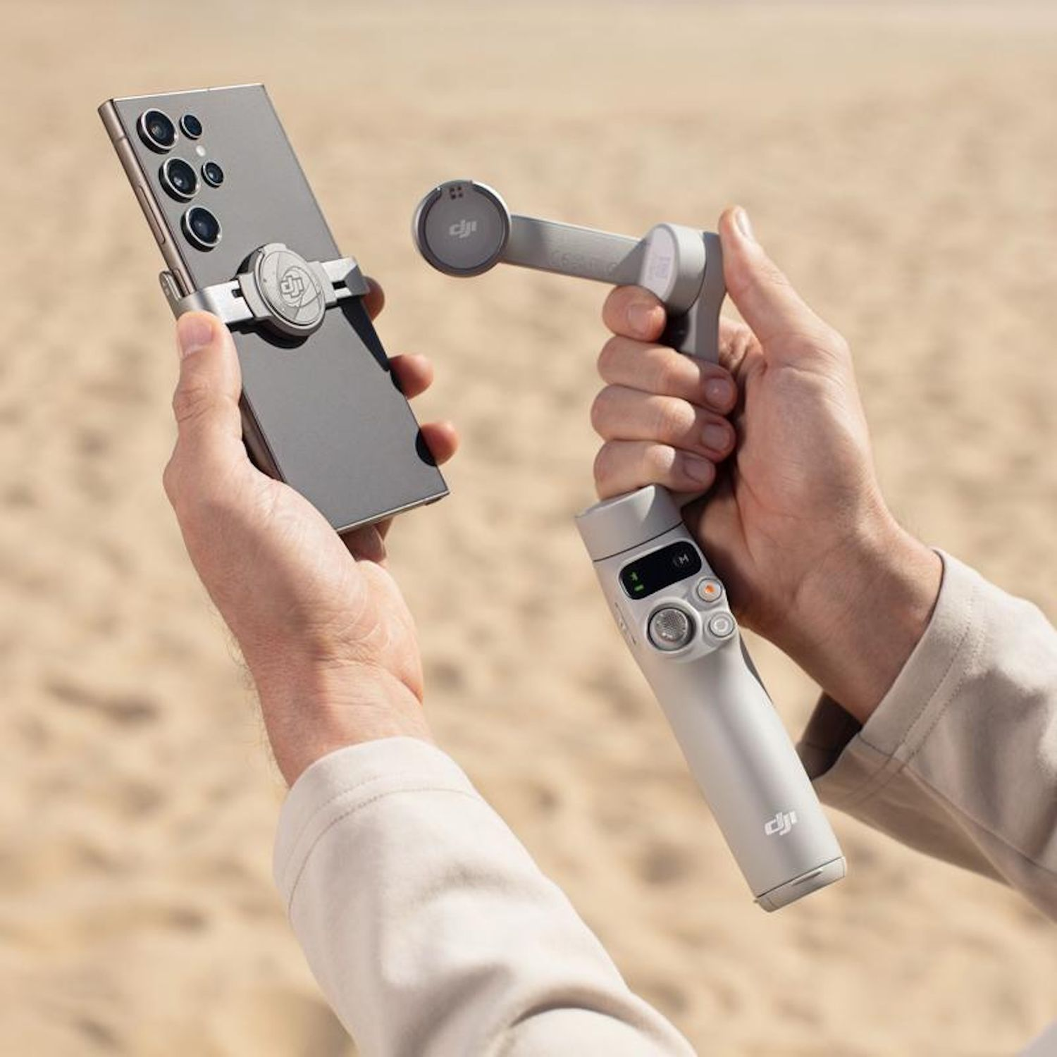Ręce trzymające szary smartfon na gimblu na tle rozmytej piaszczystej plaży.