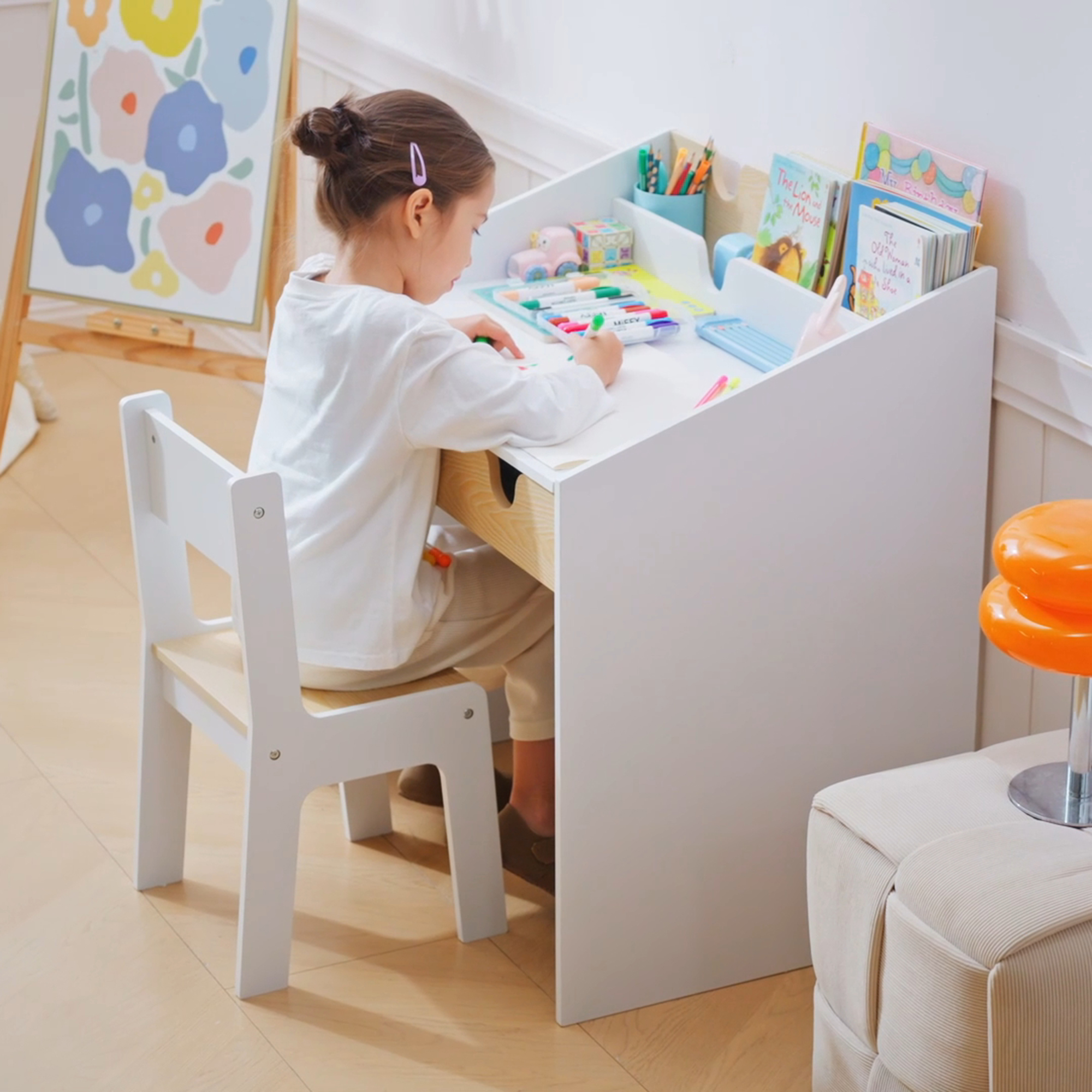 Una niña pequeña está sentada en un escritorio blanco para niños, dibujando con rotuladores de colores.