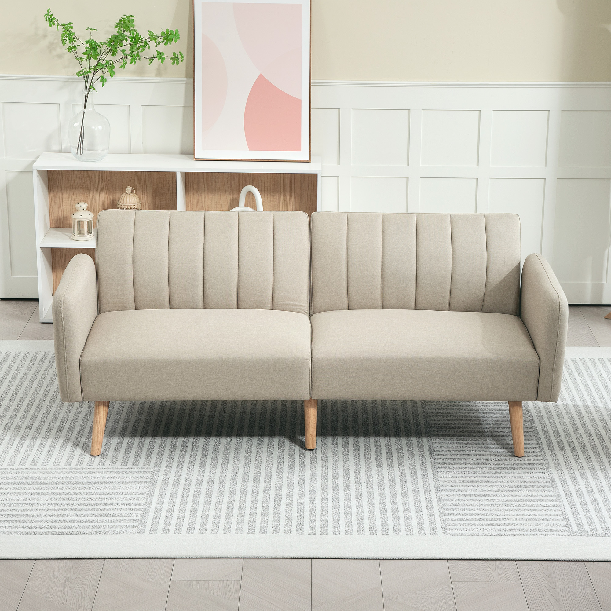 Sofá cama beige sobre alfombra de rayas blanco y gris, con estantería y cuadro al fondo.