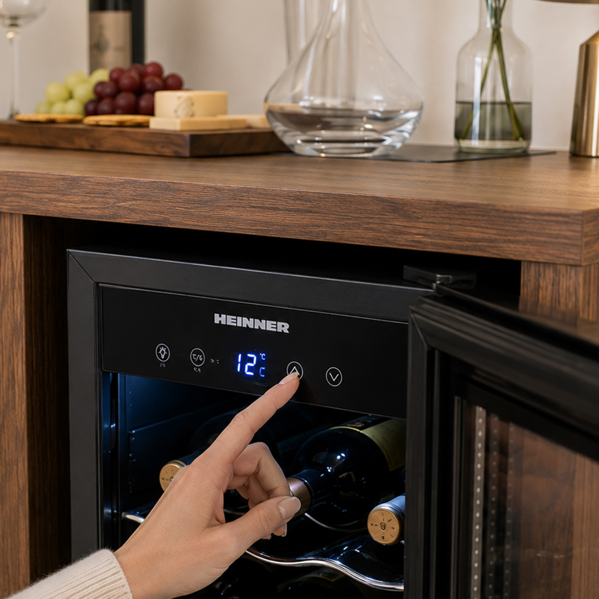 Eine Hand drückt die digitale Temperaturregelung an einem Heinner Weinkühlschrank mit Flaschen.