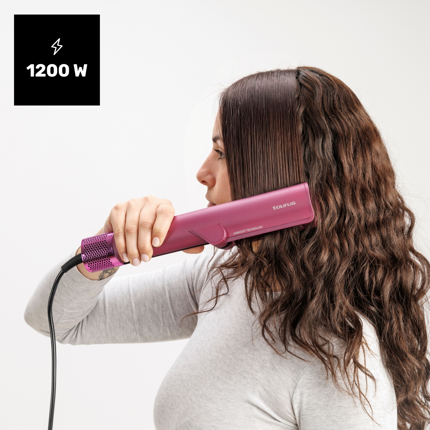 Una mujer peina su cabello castaño ondulado con una herramienta rosa de Taurus sobre fondo blanco.