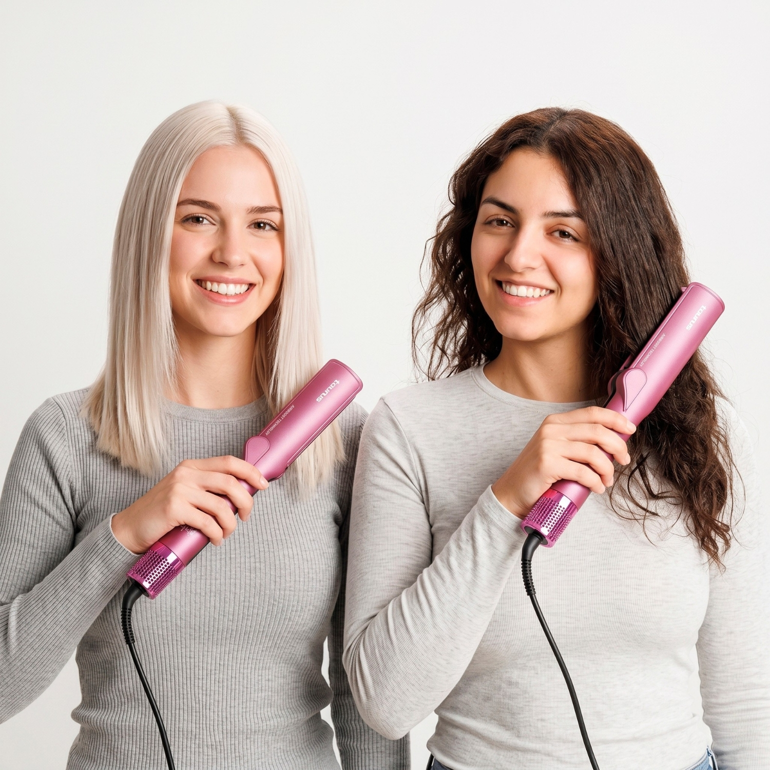 Dos mujeres sonrientes con jerséis grises sostienen planchas de pelo rosas contra un fondo blanco.