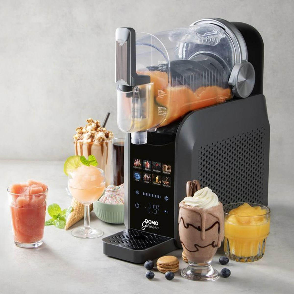 Una gelatiera nera con display digitale si trova su una superficie grigia, circondata da vari dessert e bevande.