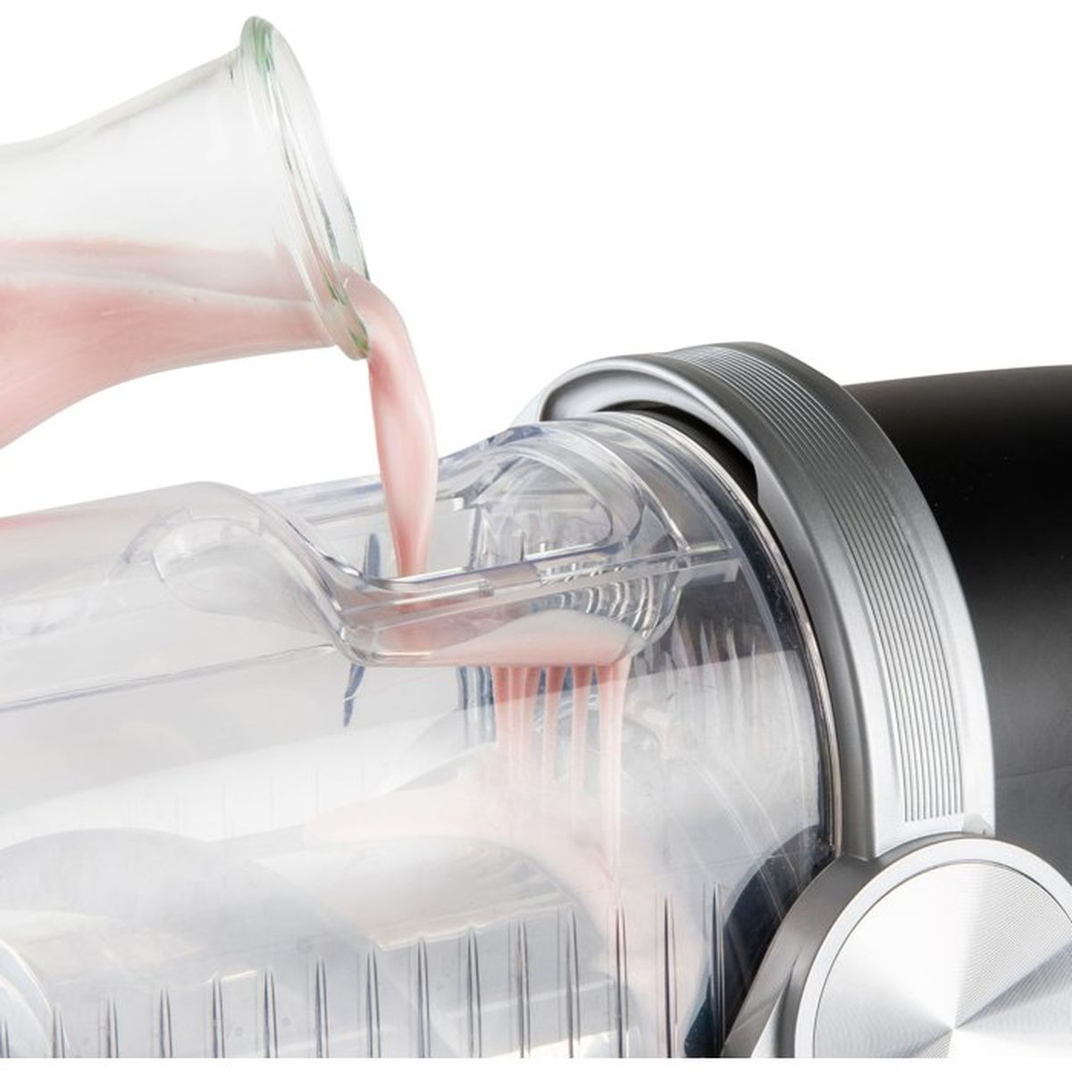 Liquido rosa versato da una brocca di vetro in un frullatore trasparente.
