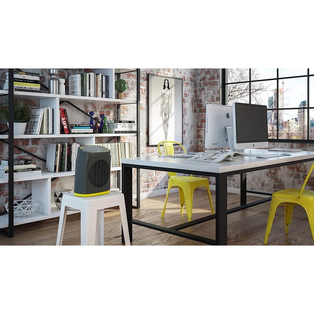 Ein raumhoher Industrieraum mit Ziegelwand, einem weißen Schreibtisch mit Computern und gelben Stühlen sowie einem Heizlüfter.