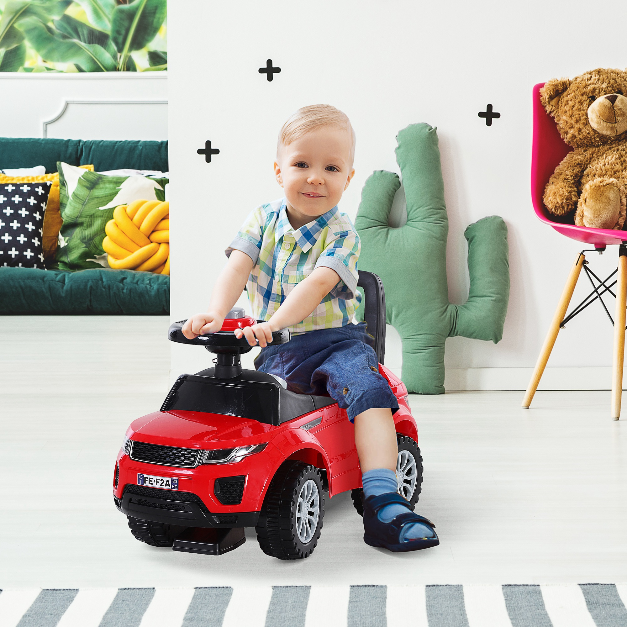 Un bambino siede su un'auto giocattolo rossa in una stanza luminosa.