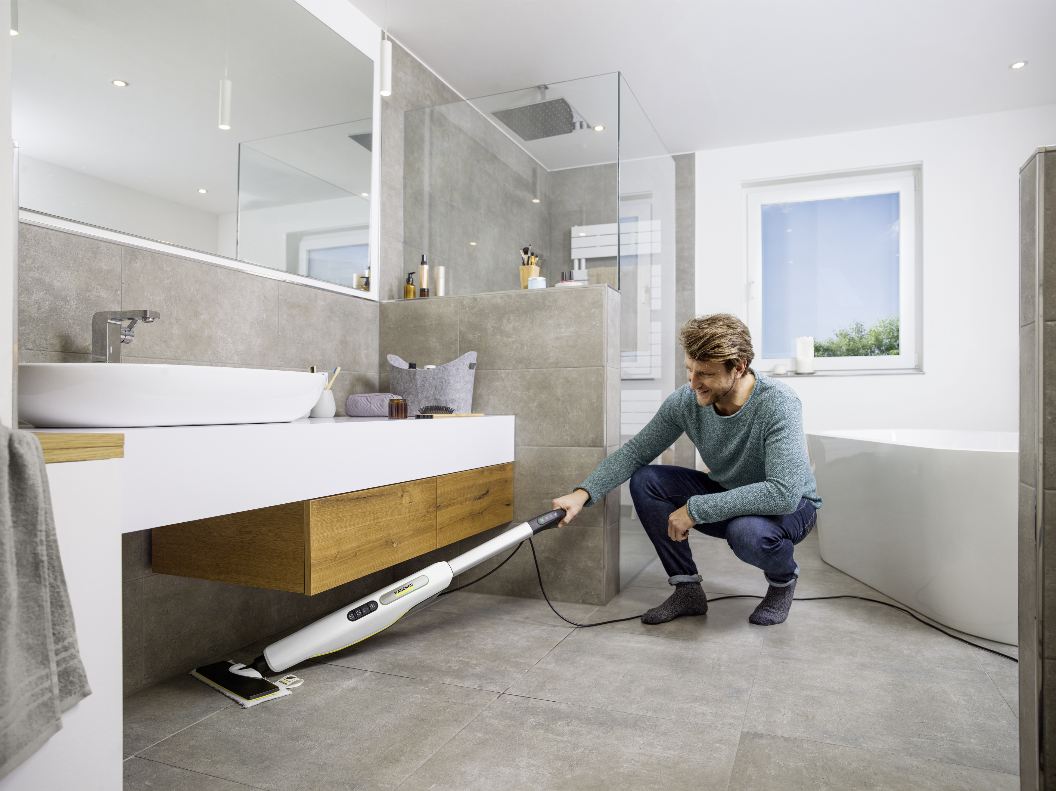 Ein Mann reinigt in einem modernen Badezimmer den Fliesenboden mit einem elektrischen Mopp.