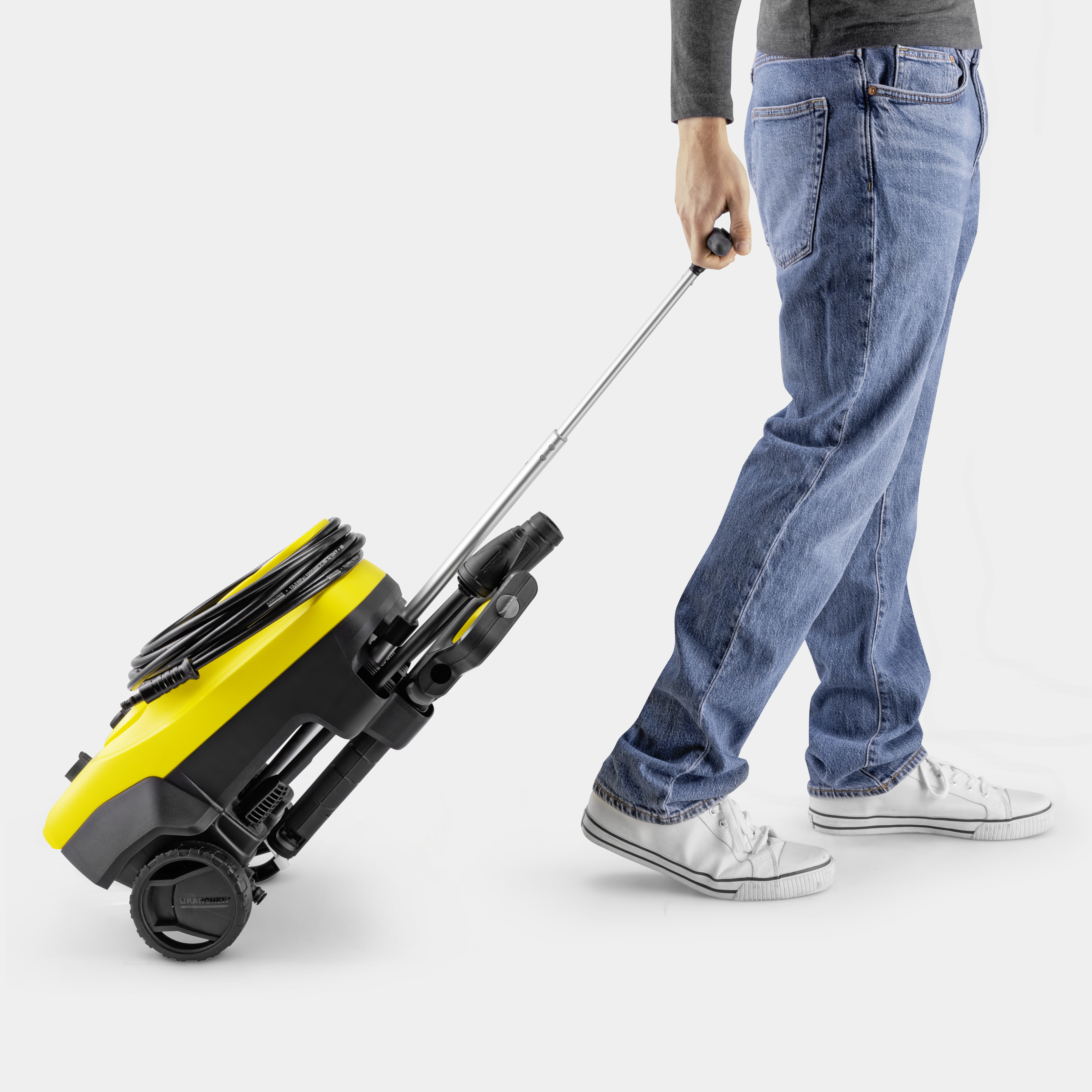 Eine Person in Jeans und weißen Schuhen zieht einen gelb-schwarzen Kärcher Hochdruckreiniger.