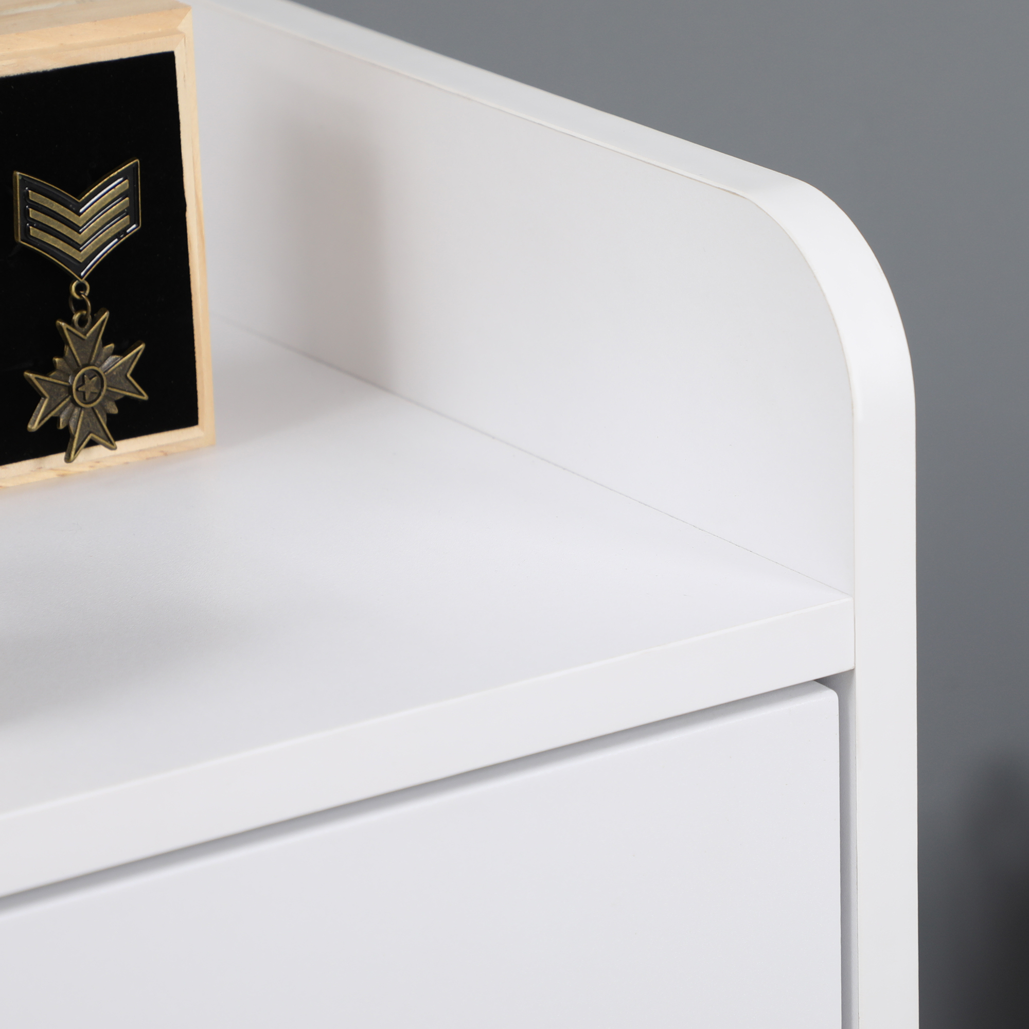 Un mueble blanco con un borde redondeado y una pequeña caja de madera que contiene una medalla militar.
