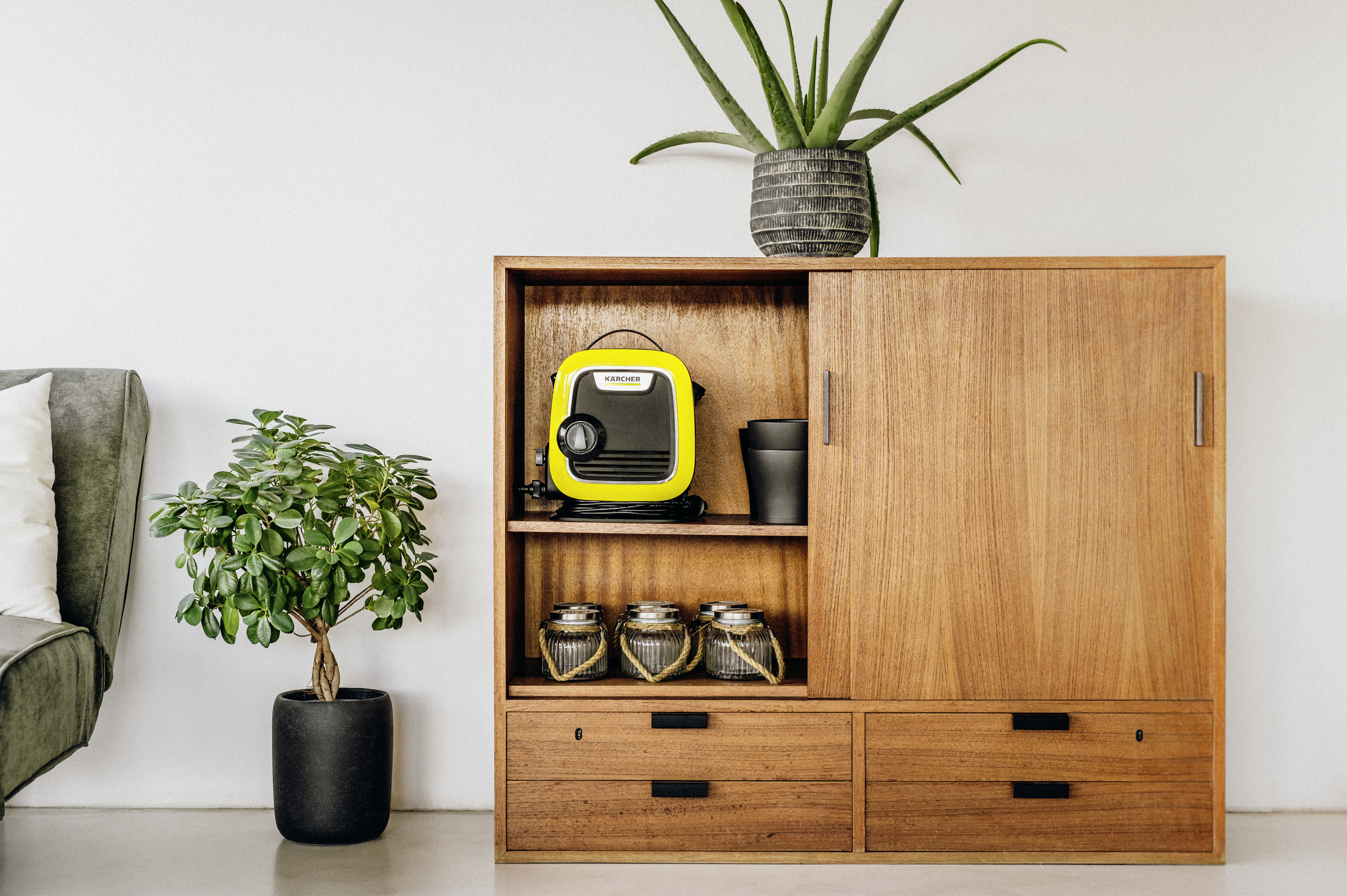 Ein Holzschrank mit einem gelben Gerät, Pflanzen und Gläsern vor einer weißen Wand.
