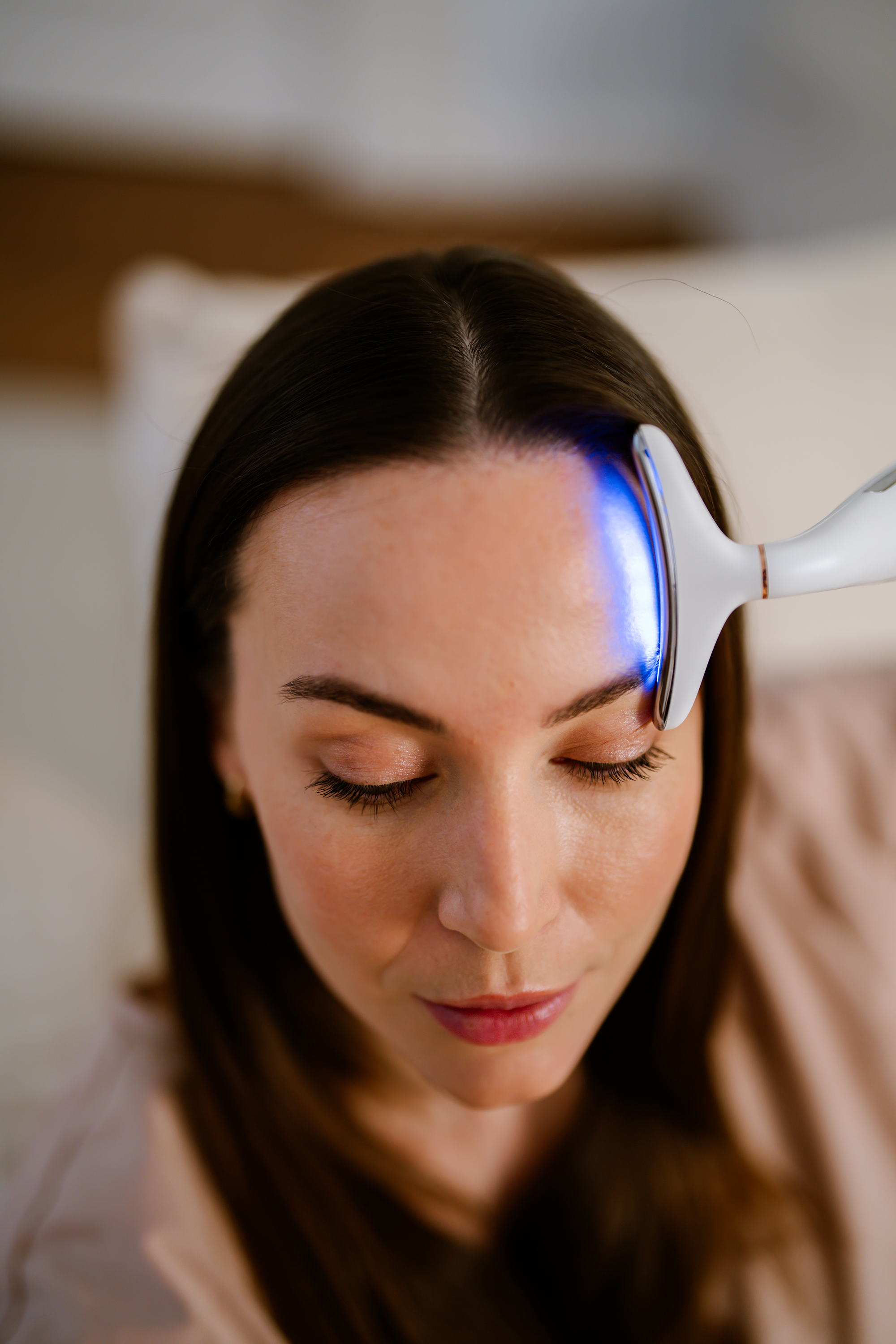 Una donna con i capelli scuri riceve un trattamento con luce blu sulla fronte.