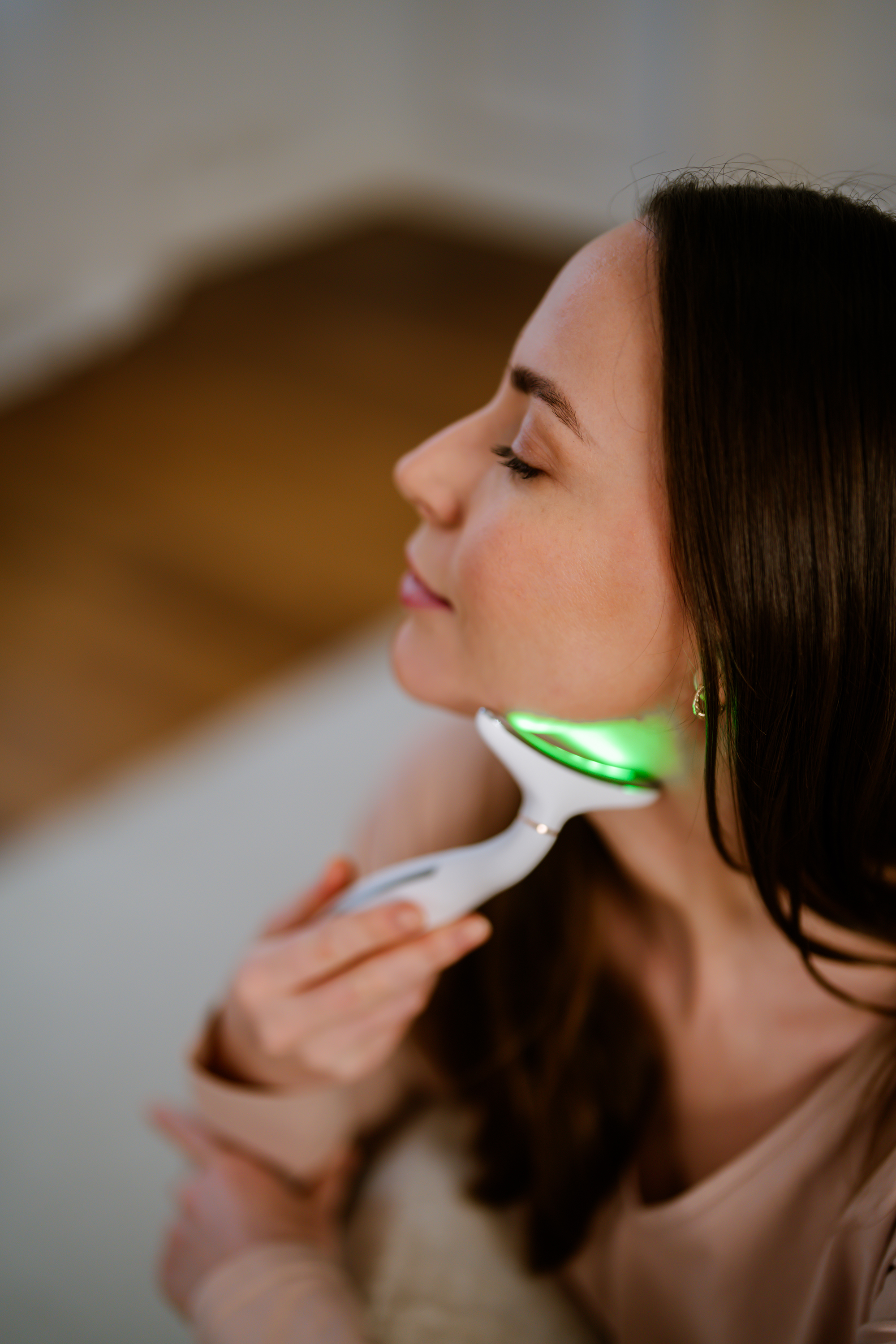 Una donna usa un dispositivo per la cura della pelle bianco con luce verde sul collo.