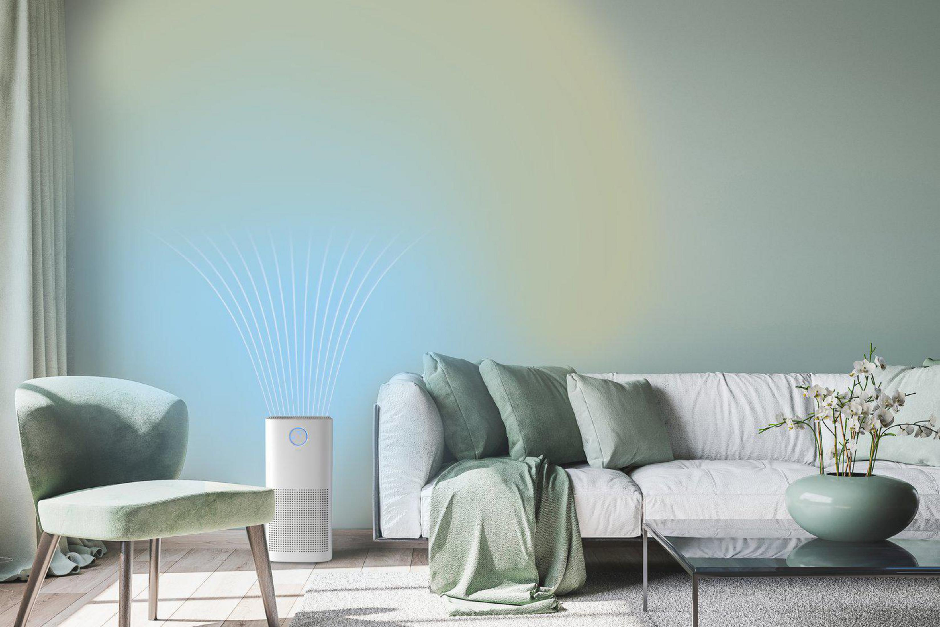 Ein weißer Luftreiniger steht neben einem Sofa in einem modern eingerichteten Wohnzimmer mit sanften Farben.