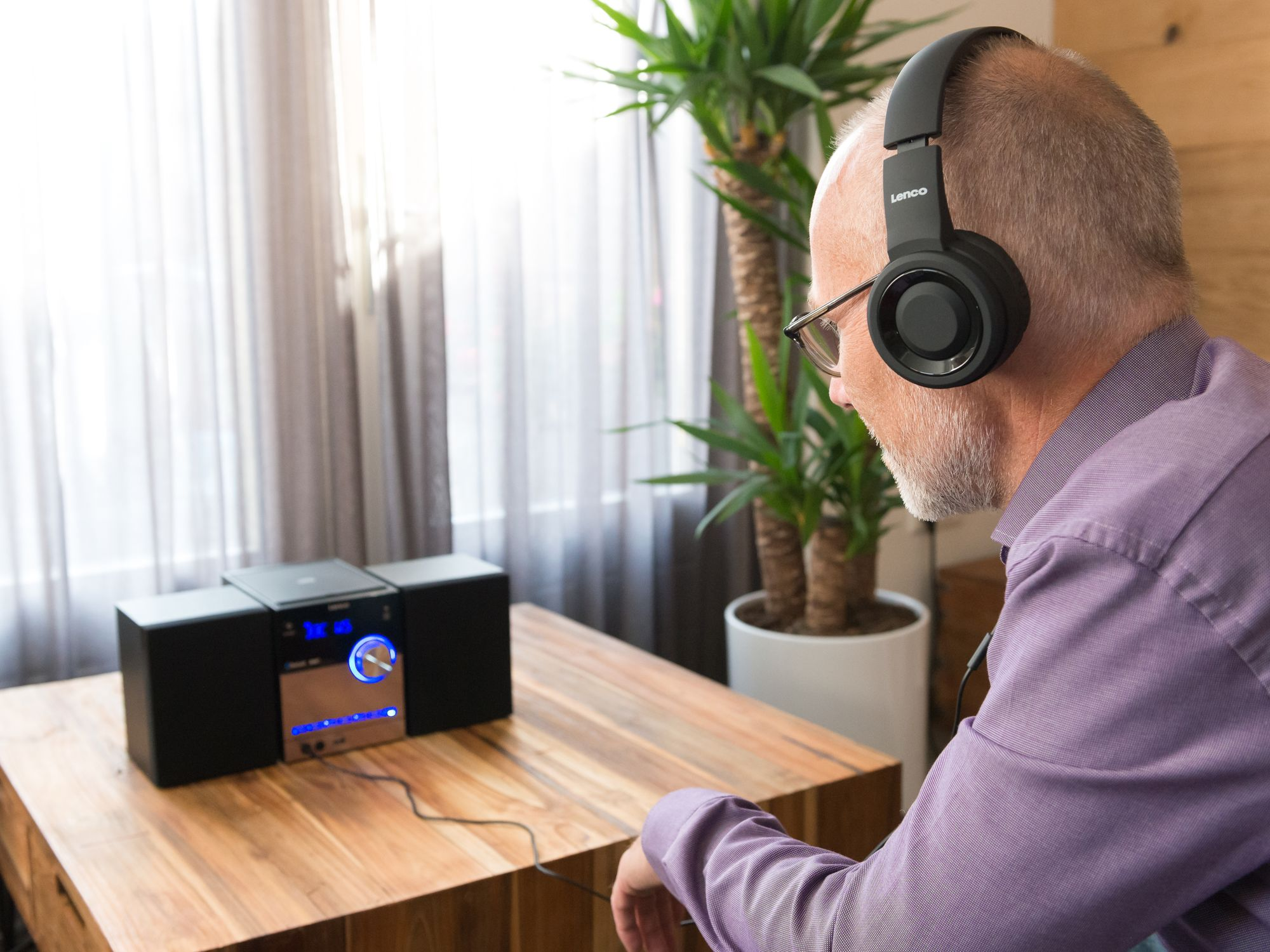 Mann mit Kopfhörern sitzt an Holztisch neben Musikanlage.