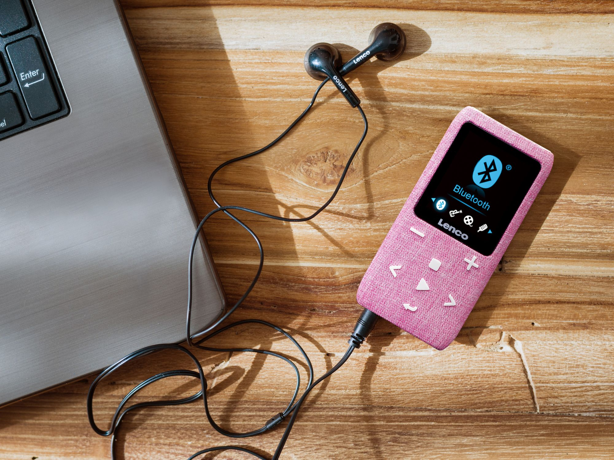 Ein pinker Lenco MP3-Player mit Kopfhörern liegt neben einem Laptop auf Holztisch.