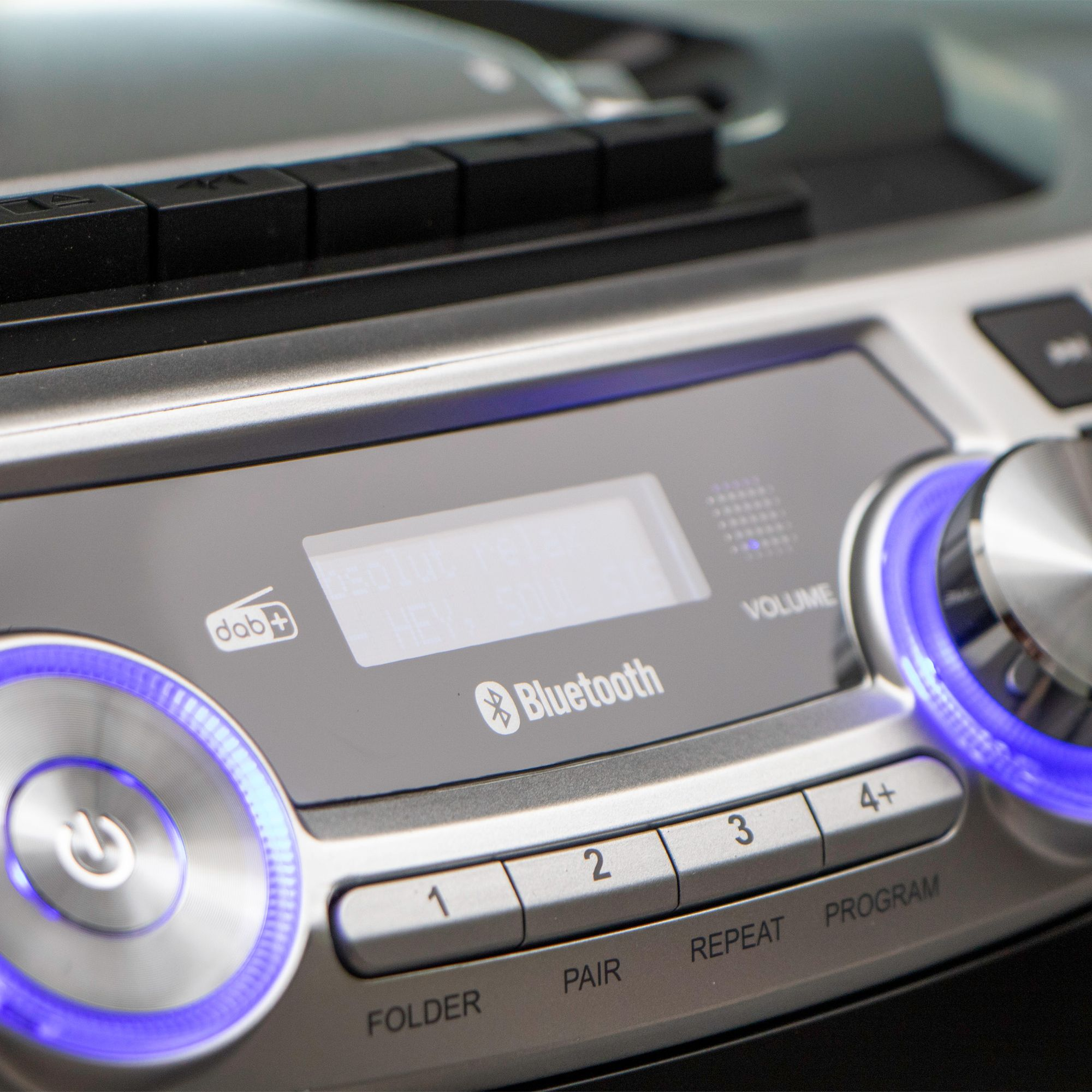 Nahaufnahme eines silbernen Audiogeräts mit blau leuchtenden Lichtern, einem Digitalbildschirm und Knöpfen.