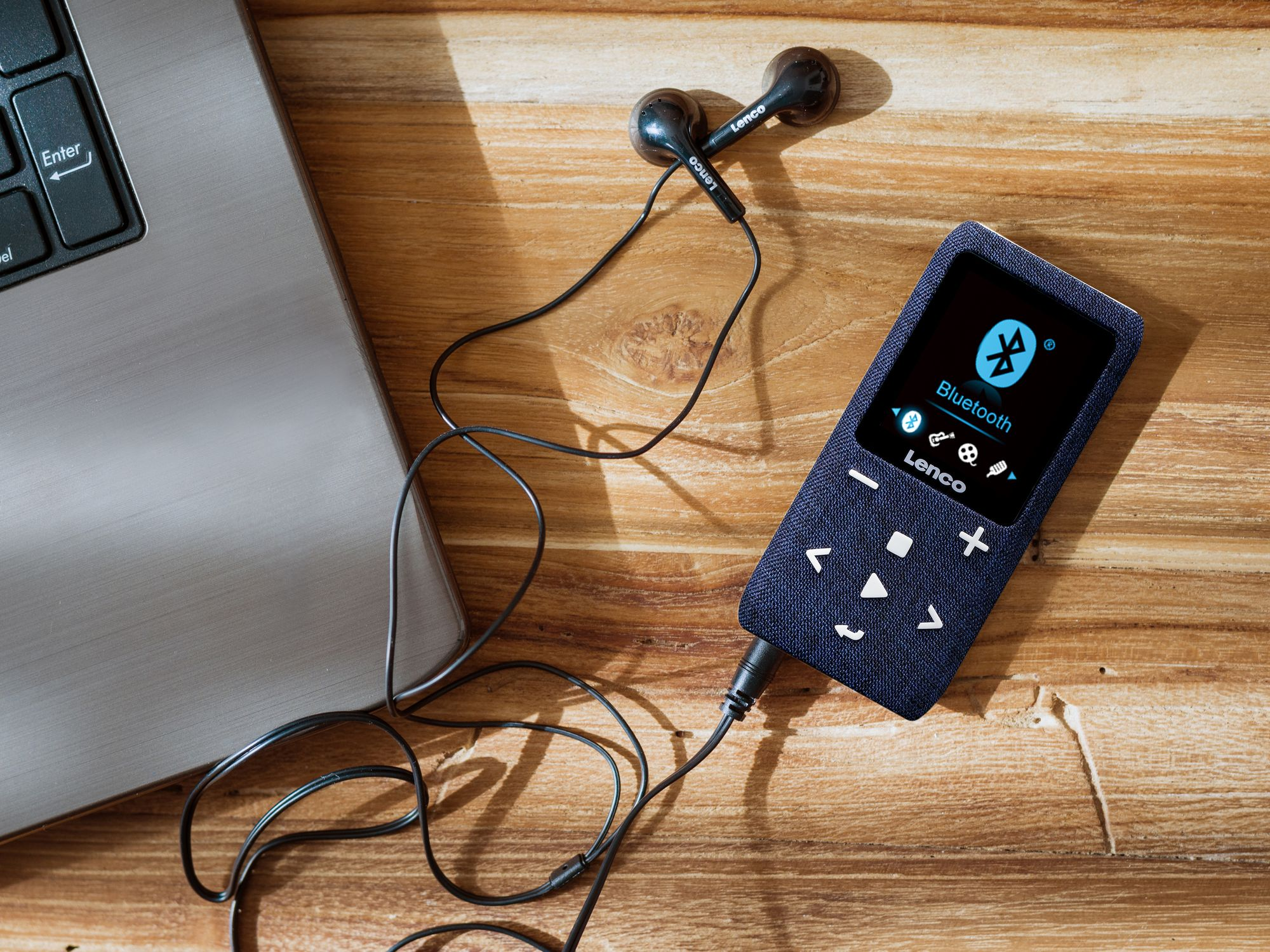 Ein blauer MP3-Player mit Kopfhörern und Laptop auf Holz.