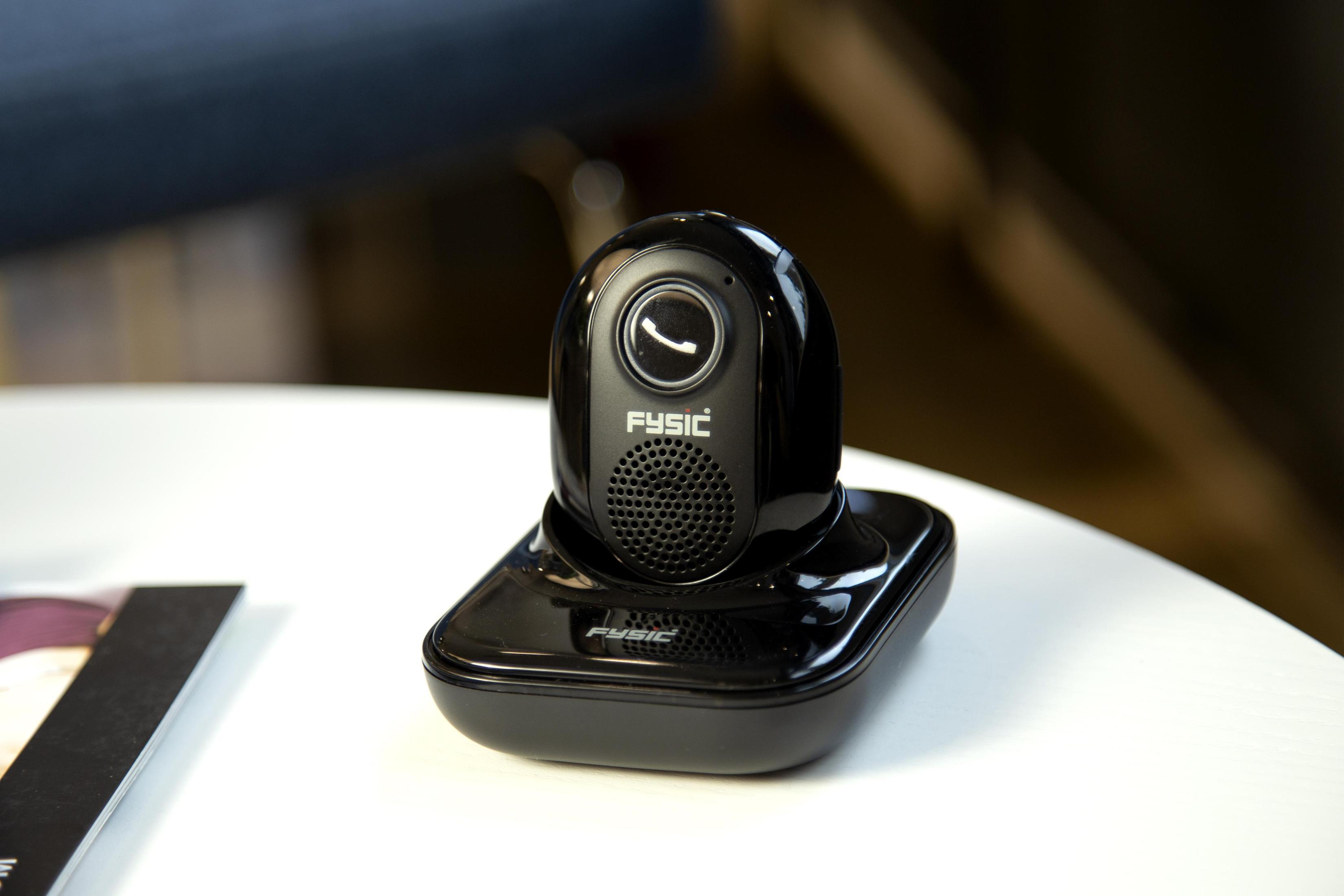 A glossy black Fysic emergency call device in its charging cradle on a white table.