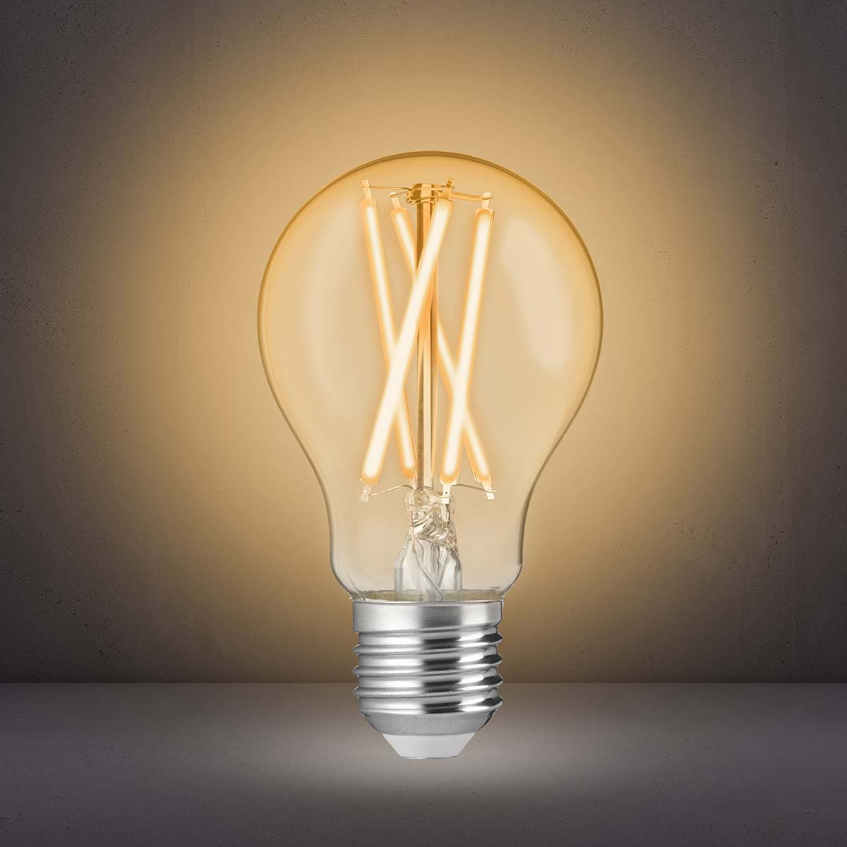 Eine eingeschaltete LED-Glühlampe mit sichtbaren Filamentfäden leuchtet vor einem grauen Hintergrund.