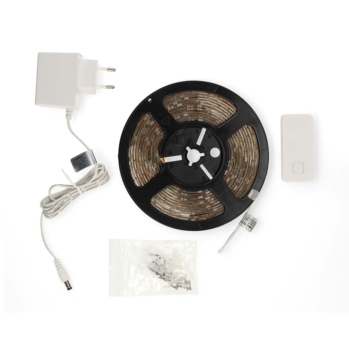 Striscia LED su bobina con alimentatore, telecomando e clip su sfondo bianco.