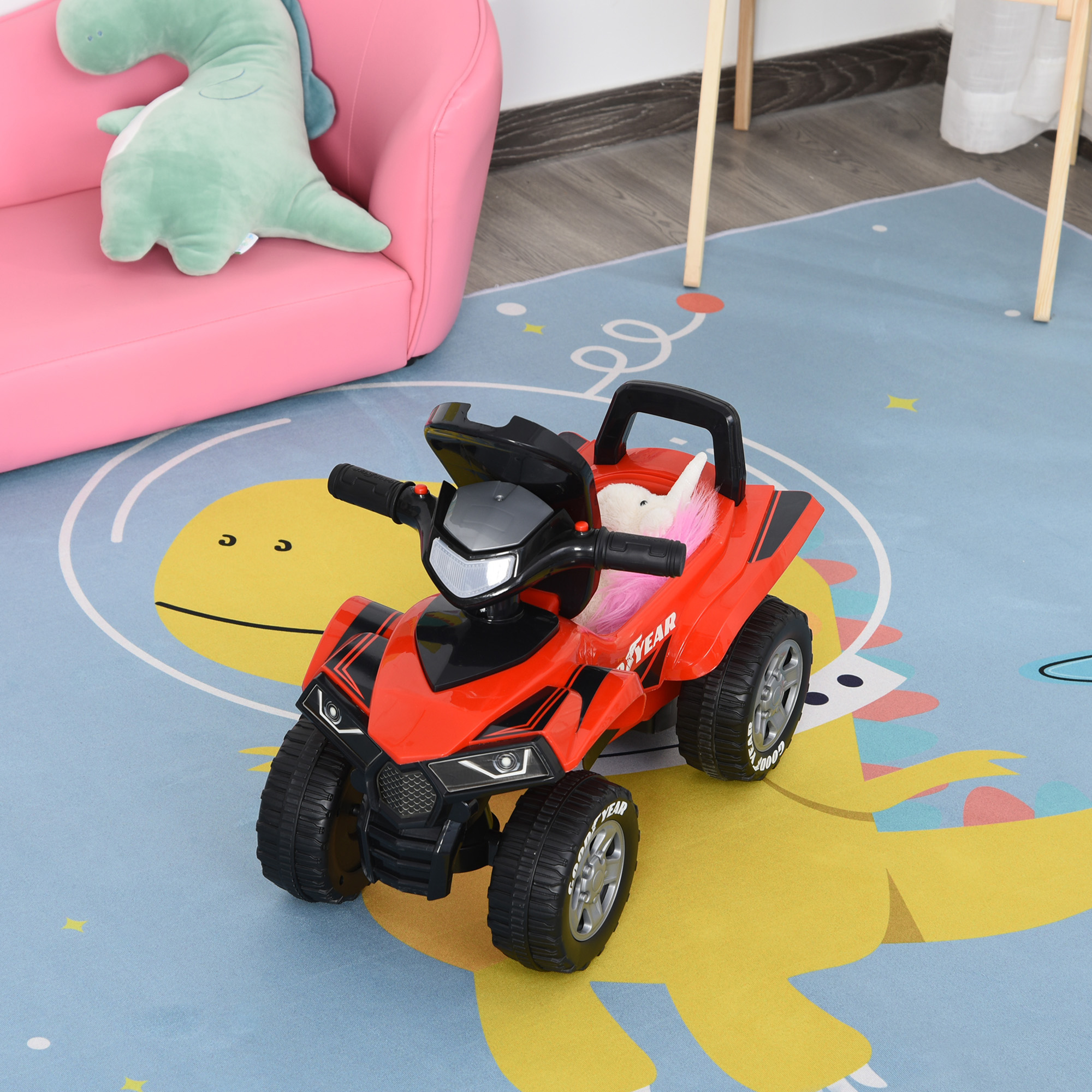 Un quad giocattolo rosso su un tappeto blu con dinosauro, con un divano rosa sullo sfondo.