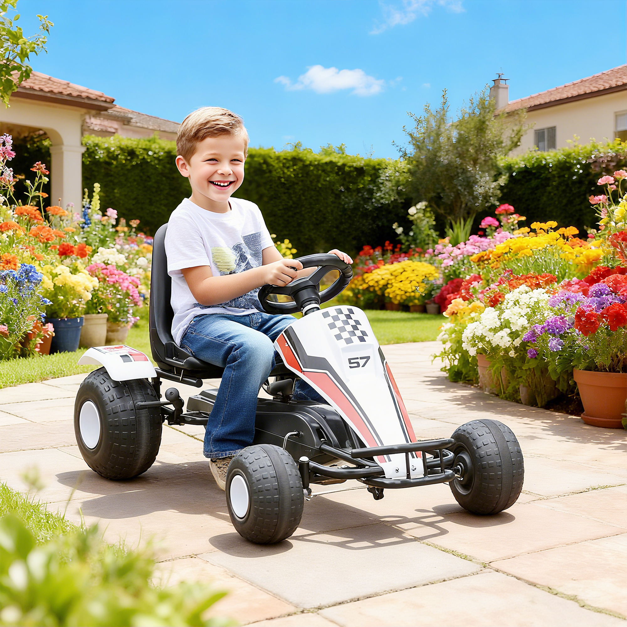 Un bambino sorridente guida un go-kart bianco e nero su un sentiero da giardino soleggiato circondato da fiori.